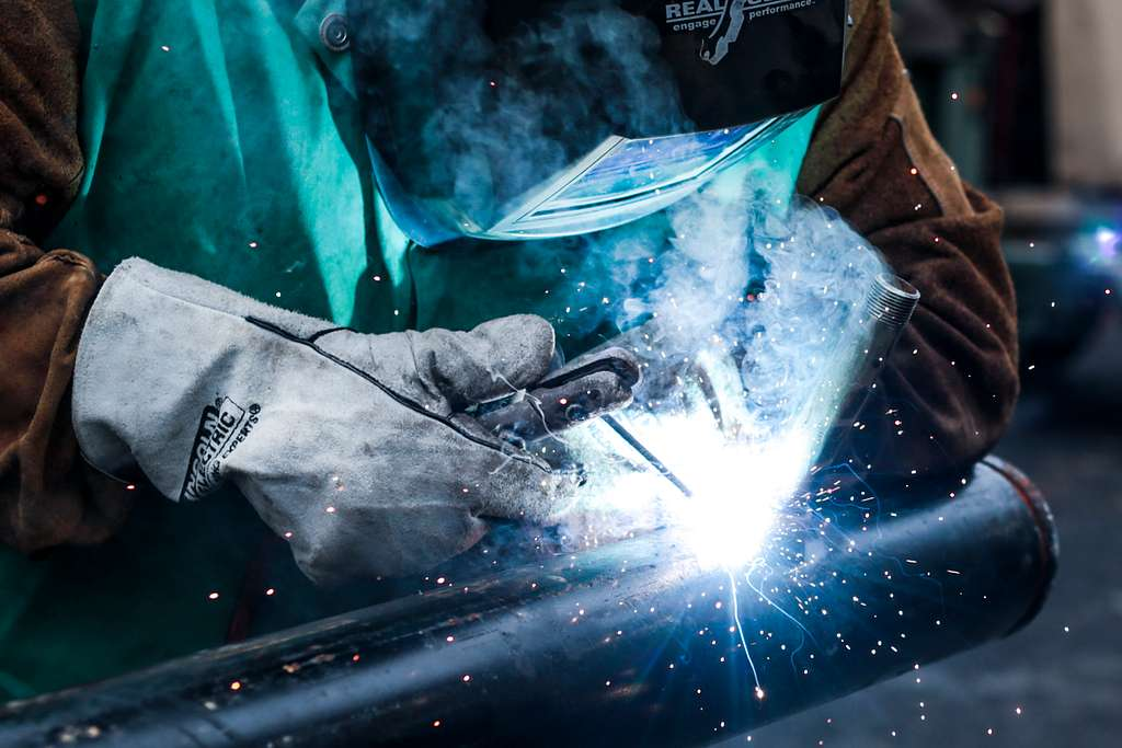 Мъж, облечен в предпазна екипировка, заварява с електрожен - поглед от близо