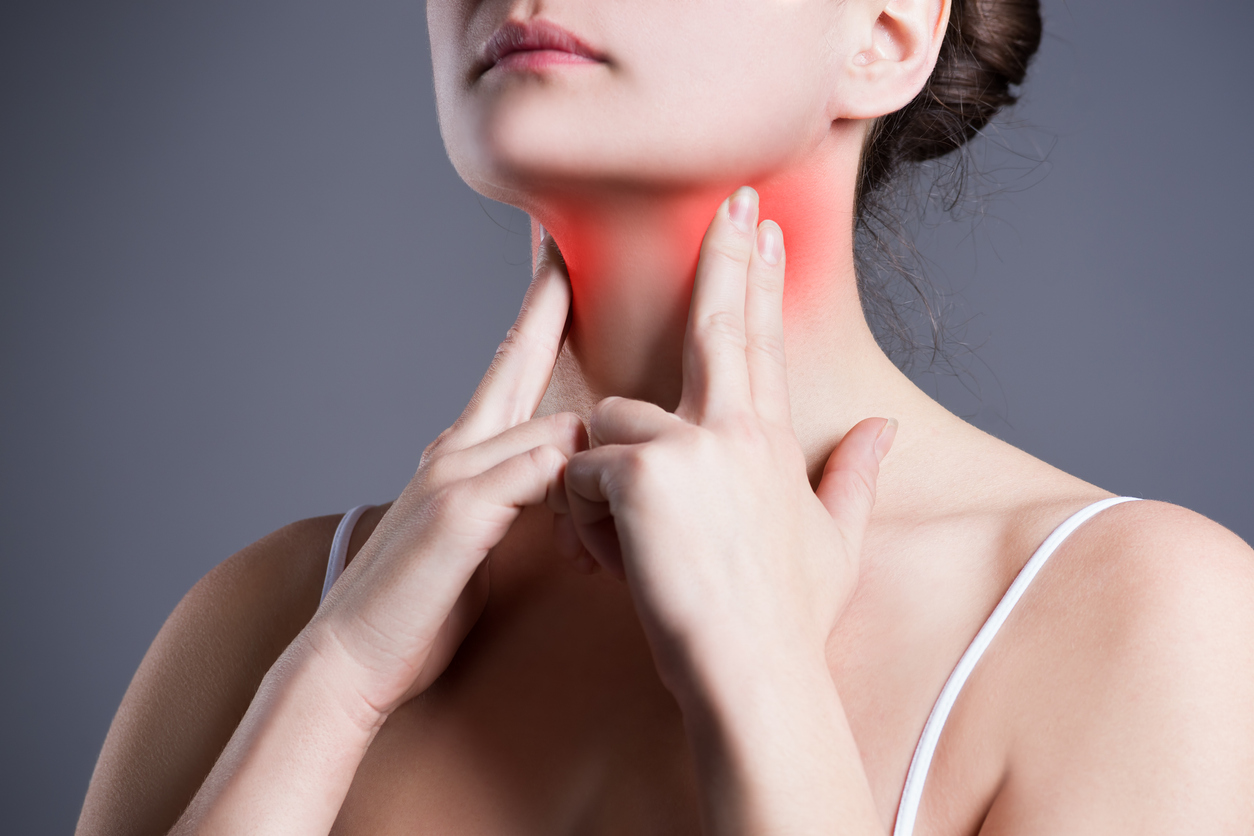 An image of a woman touching her reddened sore throat.