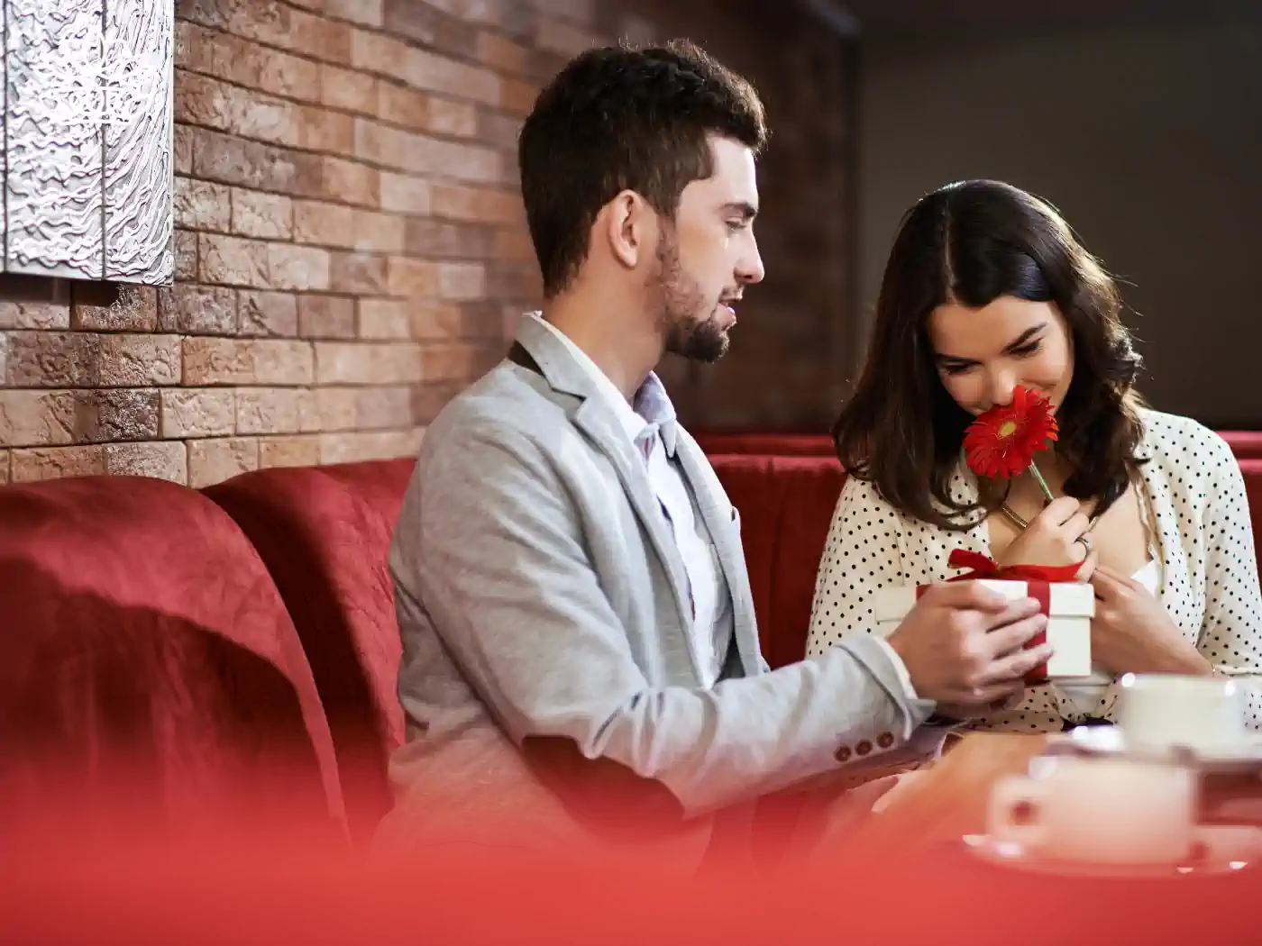 Image of a man in a restaurant giving a single red flower to a woman across the table, both looking happy. Fabulous Flowers and Gifts - Luxury Flower Bouquets.