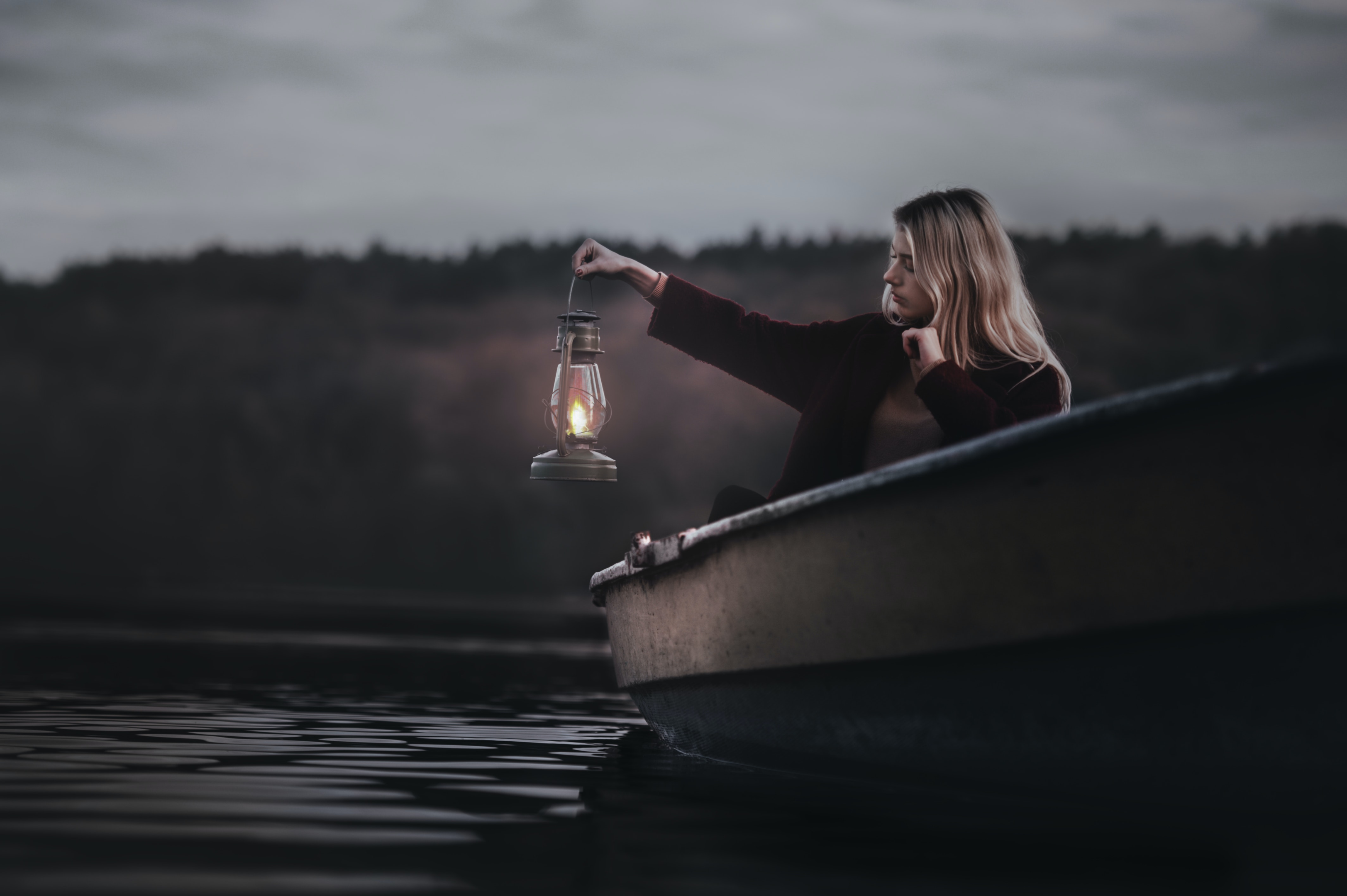 woman on a small boat in the dark, holding up a lantern