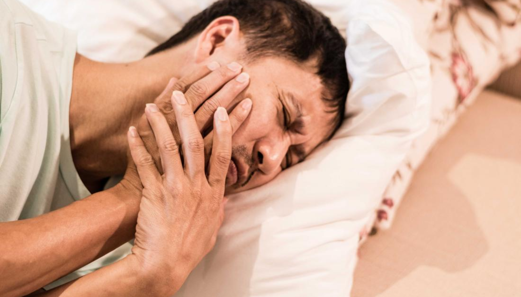 Dry Socket Varighet: Hvor Lenge Vondt Etter Tanntrekking? 12 Mann ligger i sengen og holder kjeven, tydelig smertepåvirket av tannverk eller akutte kjeveproblemer hjemme om natten alene