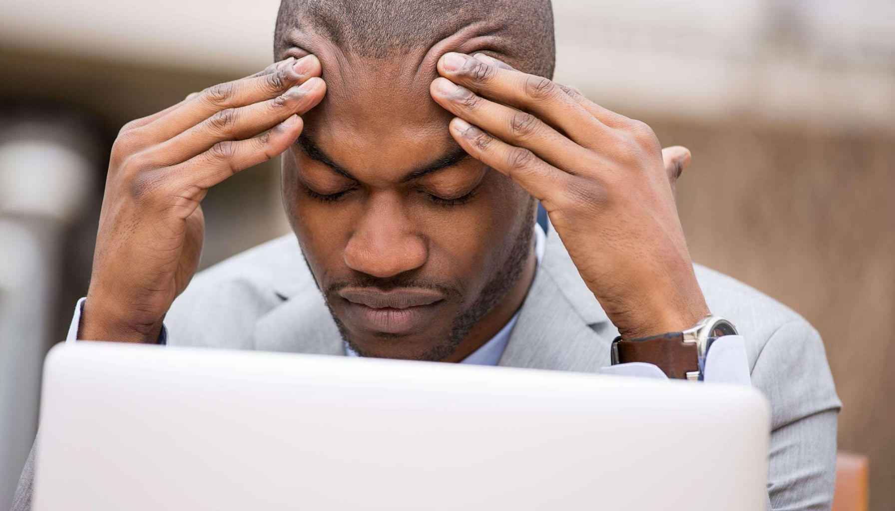 Spenningshodepine: Kan Komme Fra Kjeven 13 Alvorlig mann i dress holder tinningene mens han stirrer ned på bærbar datamaskin, tydelig stresset eller konsentrert arbeidssituasjon.