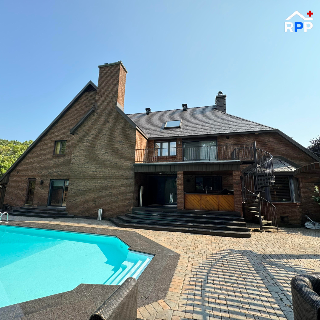 A large house featuring a swimming pool and a spacious patio and a new metal roof installation, set in a sunny outdoor environment.