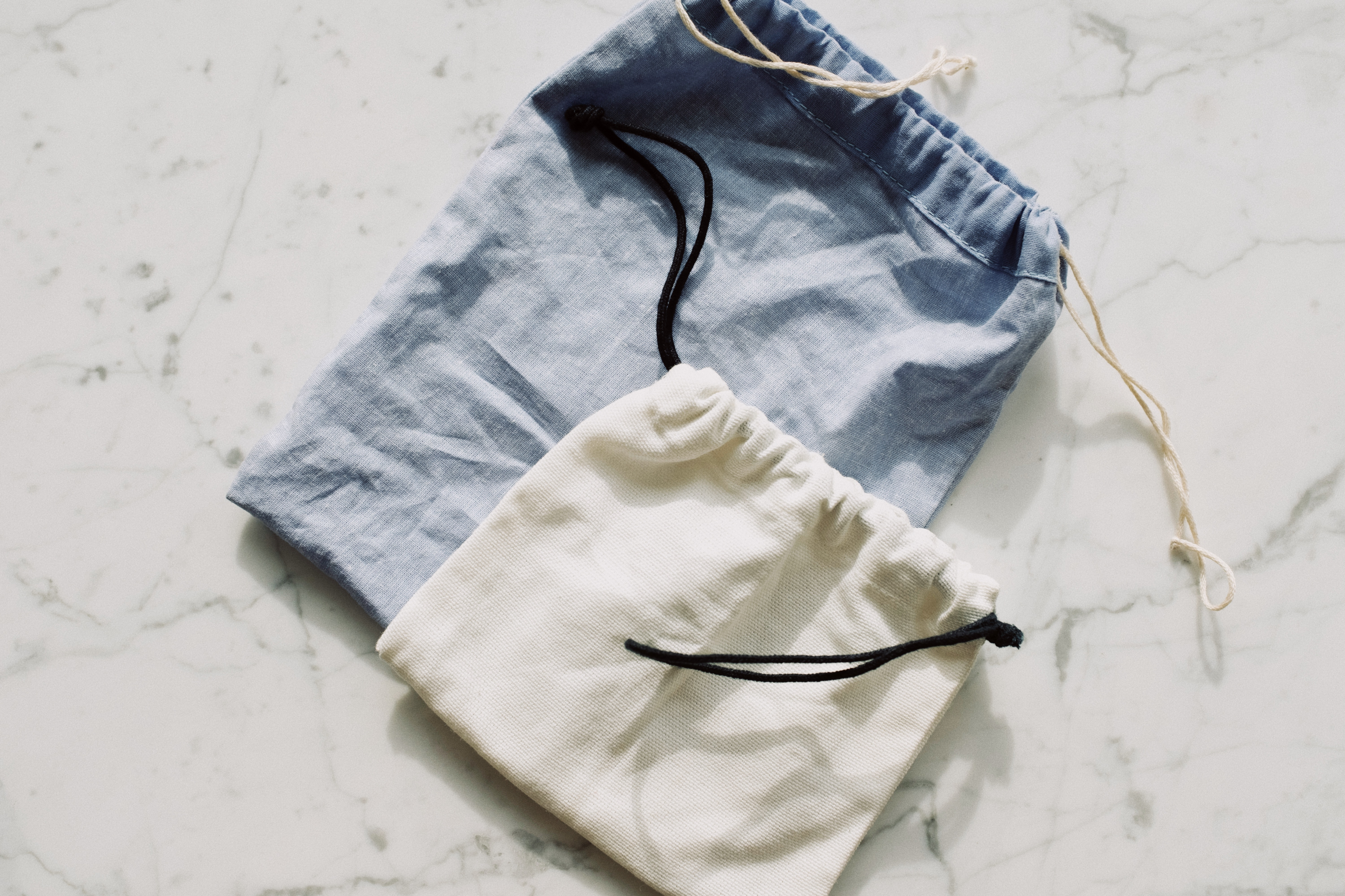 A close-up of two open pouches laid flat on a white surface, one on top of the other. The bottom pouch is larger and light-blue, while the top pouch is smaller and white.