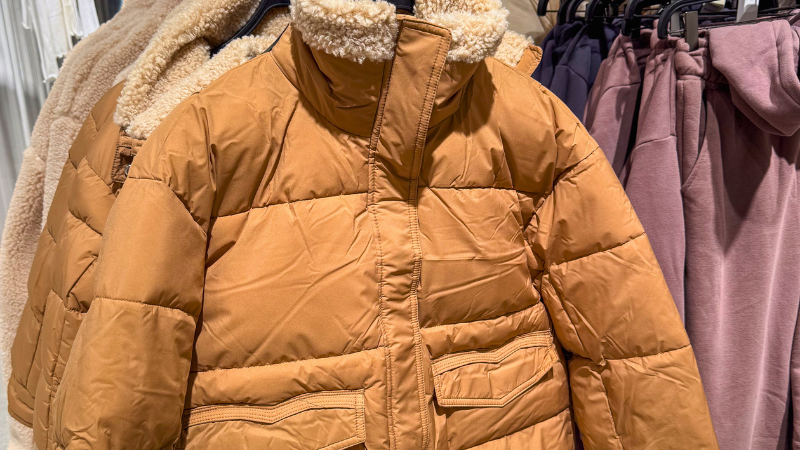 A close-up of a brown gorpcore jacket with a fluffy collar on a rack.