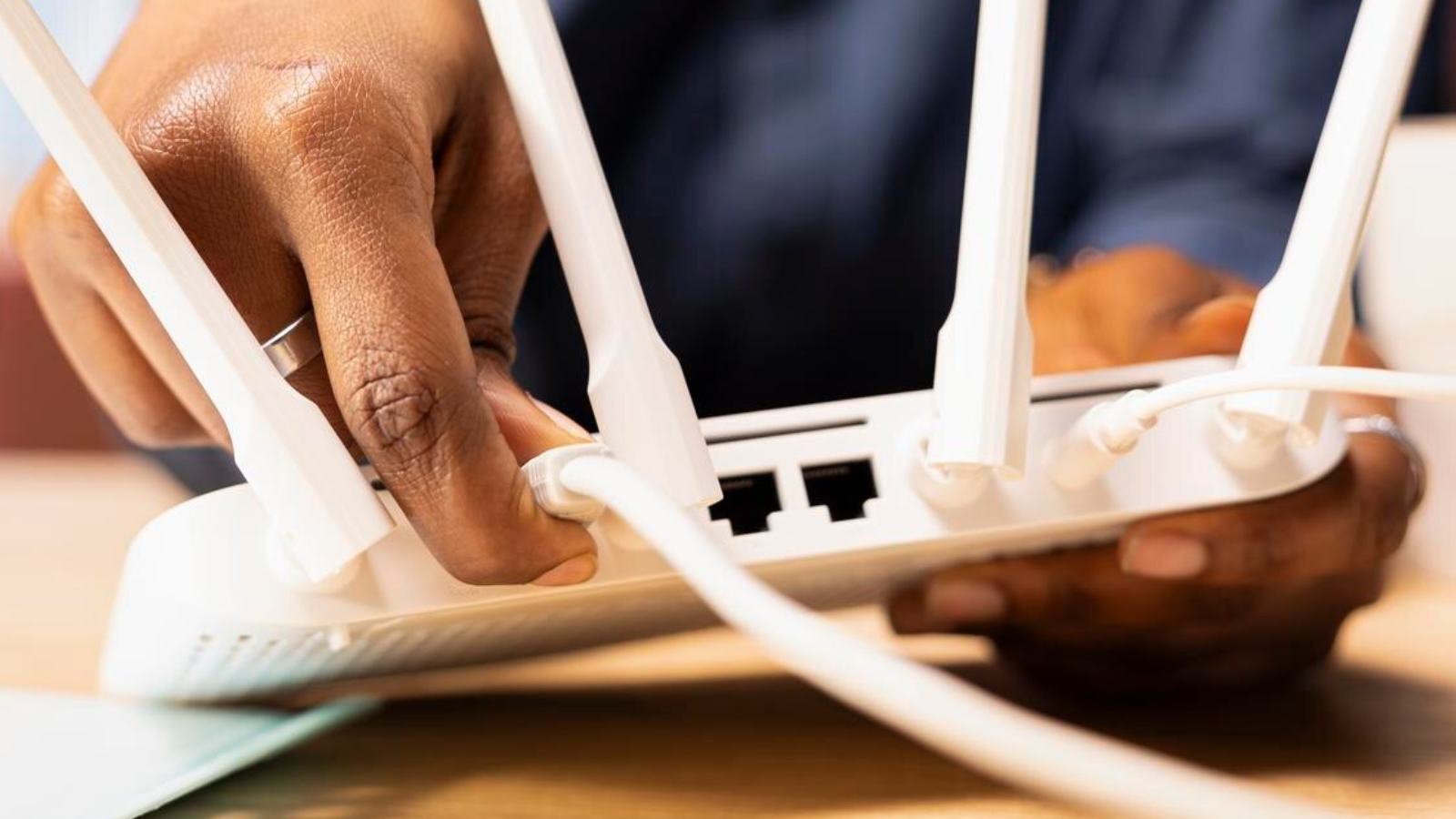 A person's hand connects a cable to a modern wireless router highlighting the kind of digital setup that powers reliable replacement for analog POTS lines like the ones found in alarms and elevator phones.