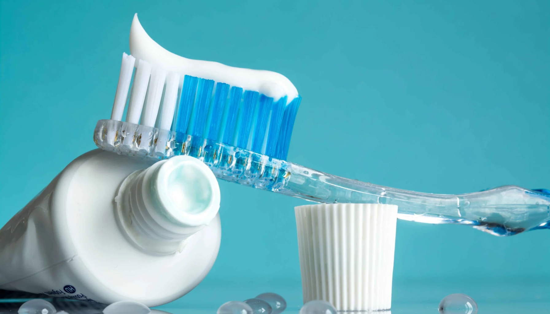 Tannkrem mot ising: Slik finner du riktig type 15 "Tannbørste med blå bust og hvit tannkrem balansert på tannkremtube mot blå bakgrunn."