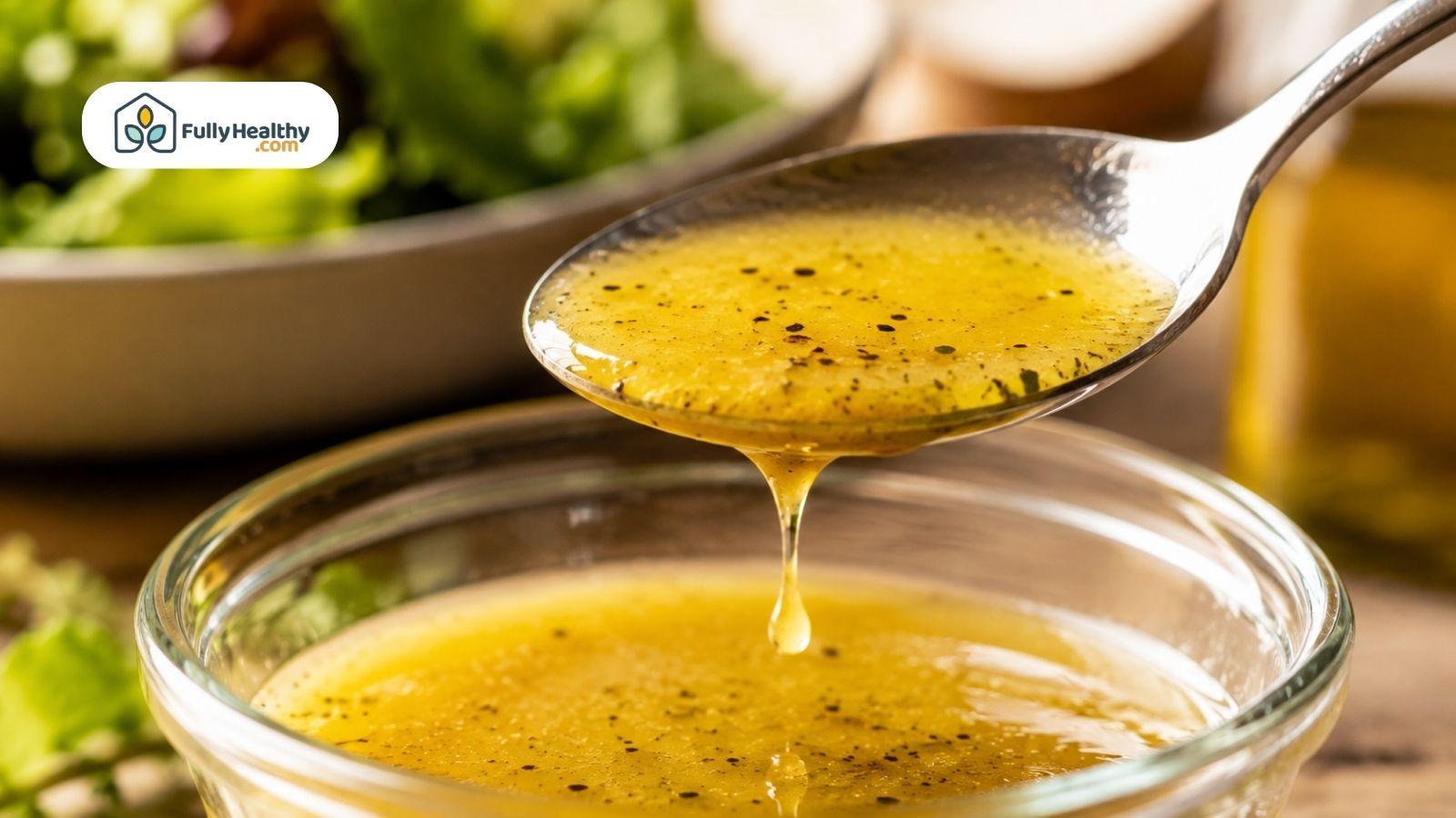 Vinaigrette dressing dripping from spoon above bowl with fresh greens.