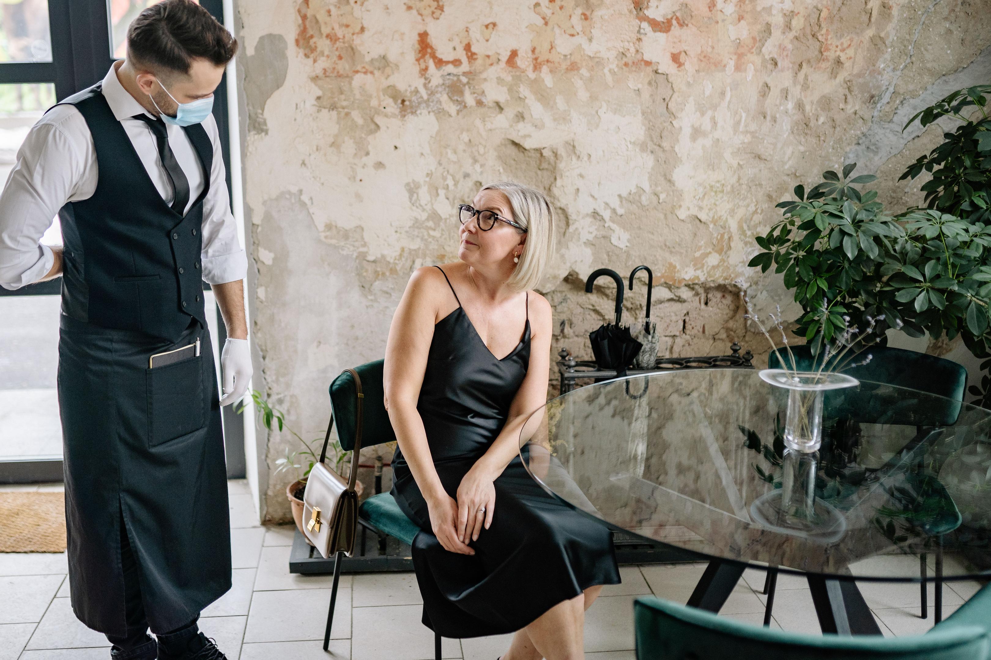 The image depicts a calm restaurant dining room where a server is attentively engaging with seated guests, highlighting the importance of excellent customer service in the restaurant industry. This scene reflects effective restaurant management, showcasing the server's role in enhancing the dining experience and fostering a positive work environment.