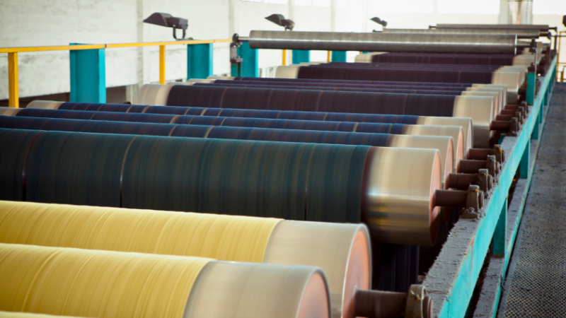 Many rolls of fabric are lined up on a conveyor belt
