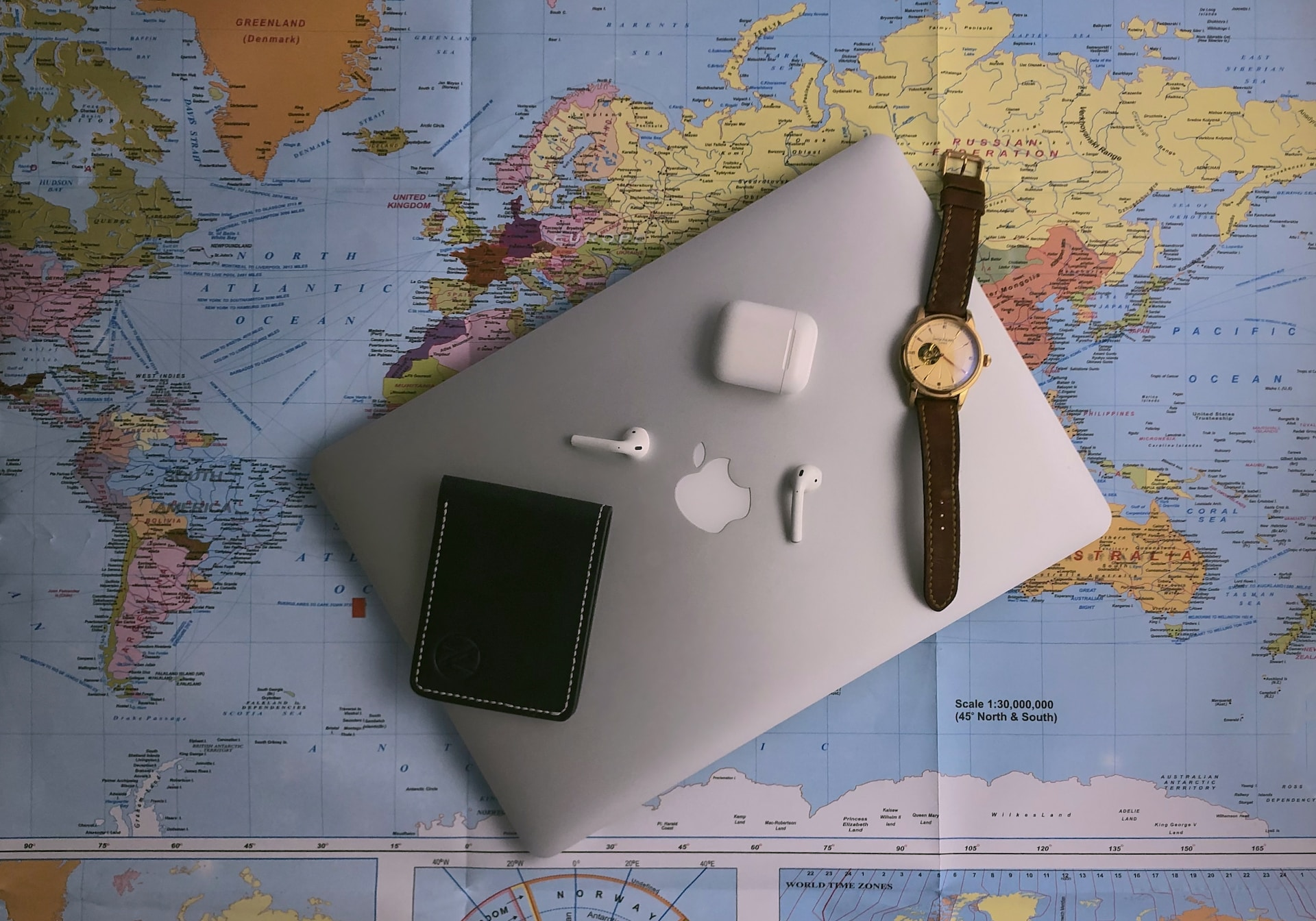 Photo of a laptop device, ear pods and watch on top of a world map to illustrate packing for a cottage holiday 