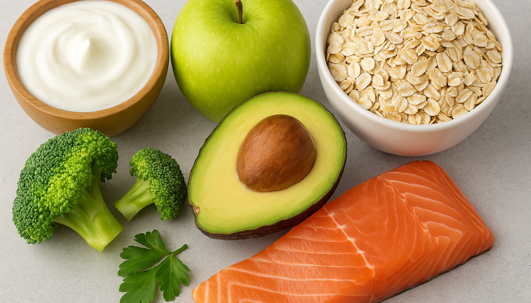 Sunne matvarer som avokado, laks, yoghurt, eple, brokkoli og havre arrangert på bordflate uten tekst.