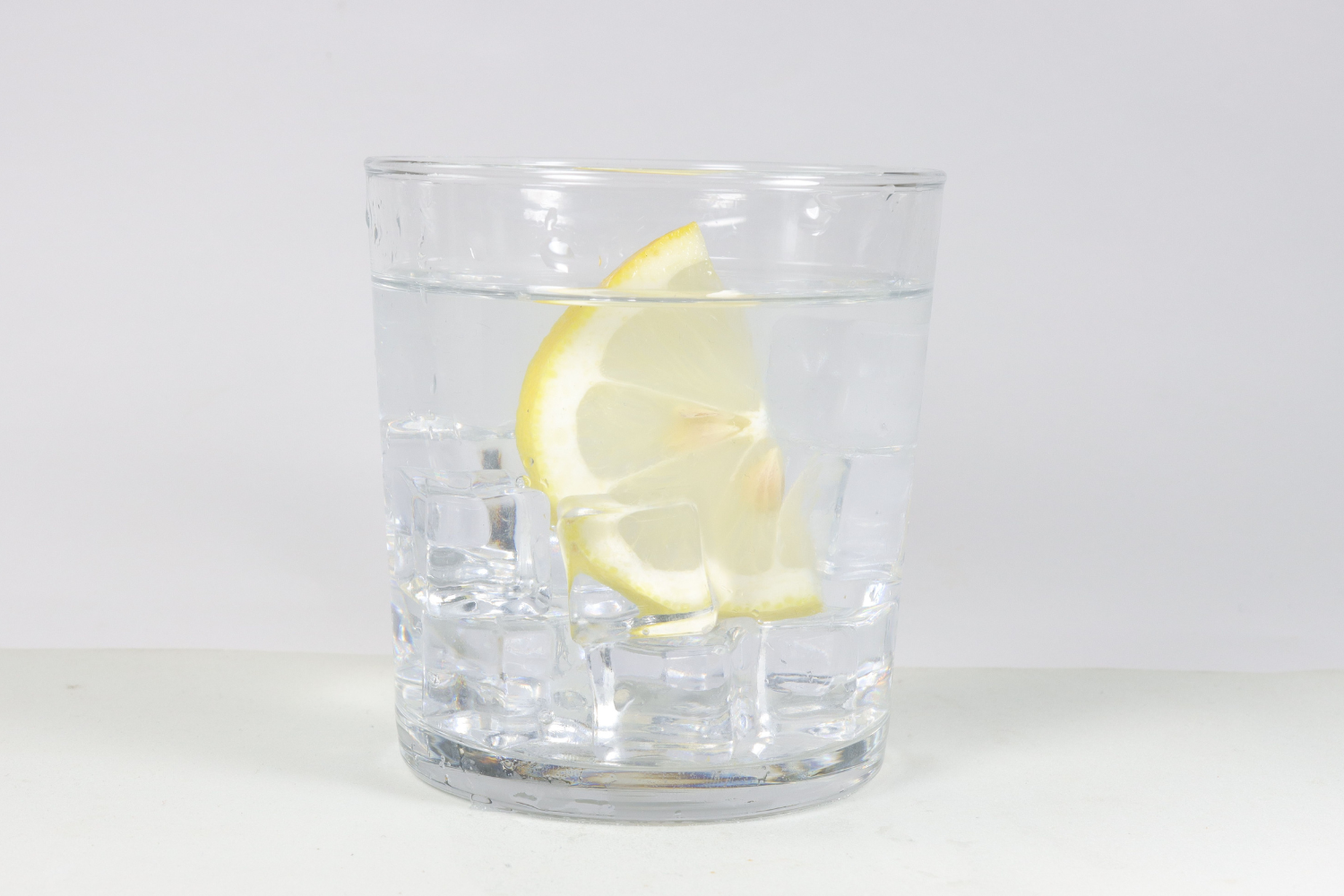 Clear glass of electrolyte drink with lemon wedge.