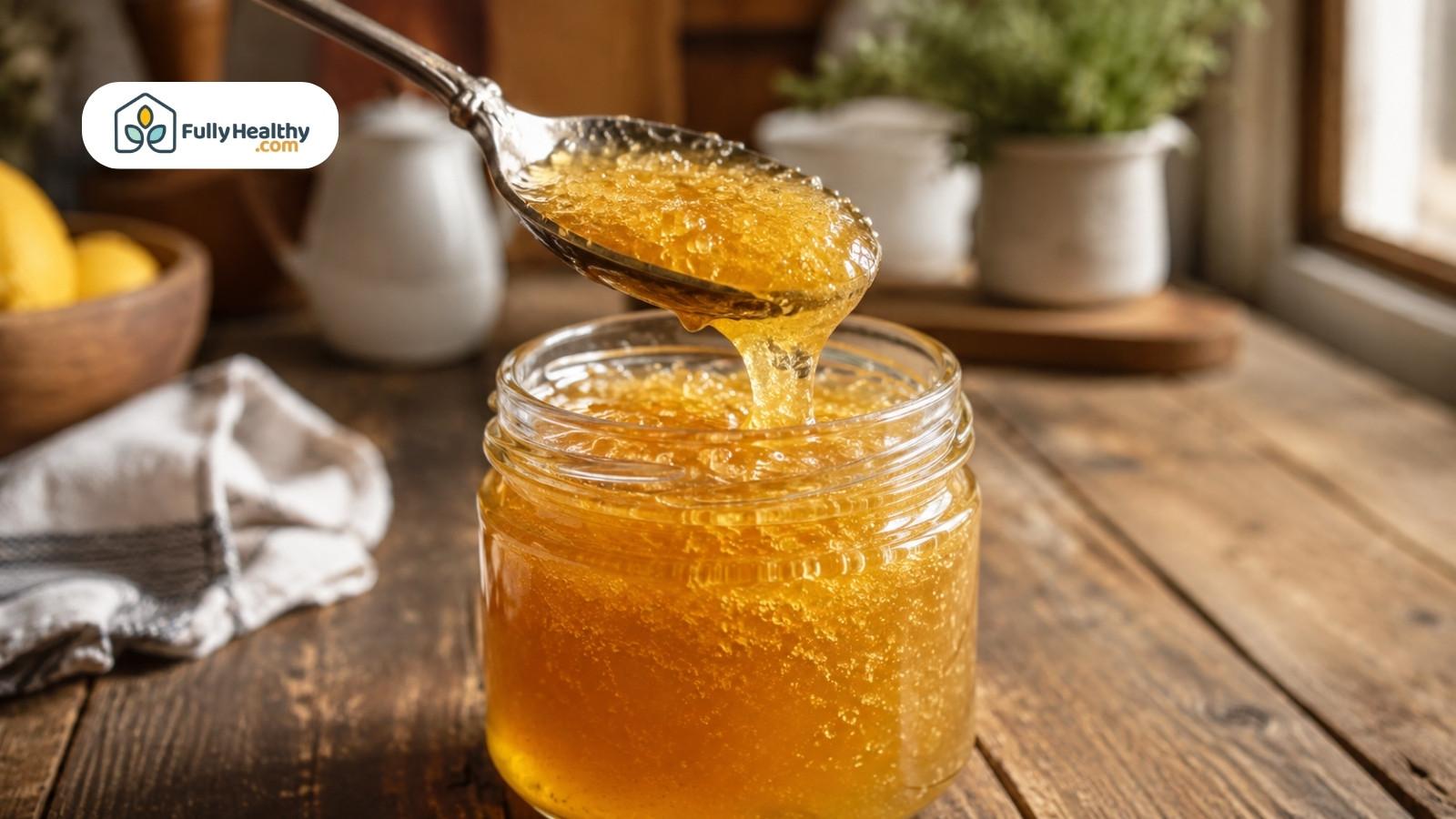 Spoon dripping crystallized honey into jar on rustic wooden kitchen table