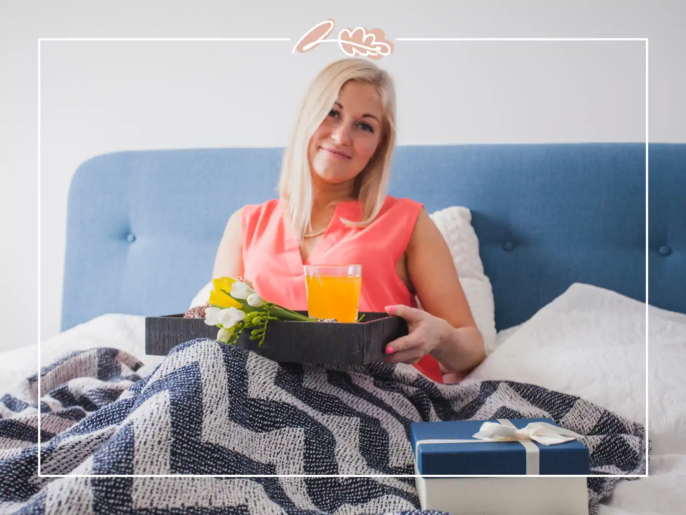 Blonde woman in bed with a tray holding orange juice and flowers, next to a blue gift box, Fabulous Flowers and Gifts