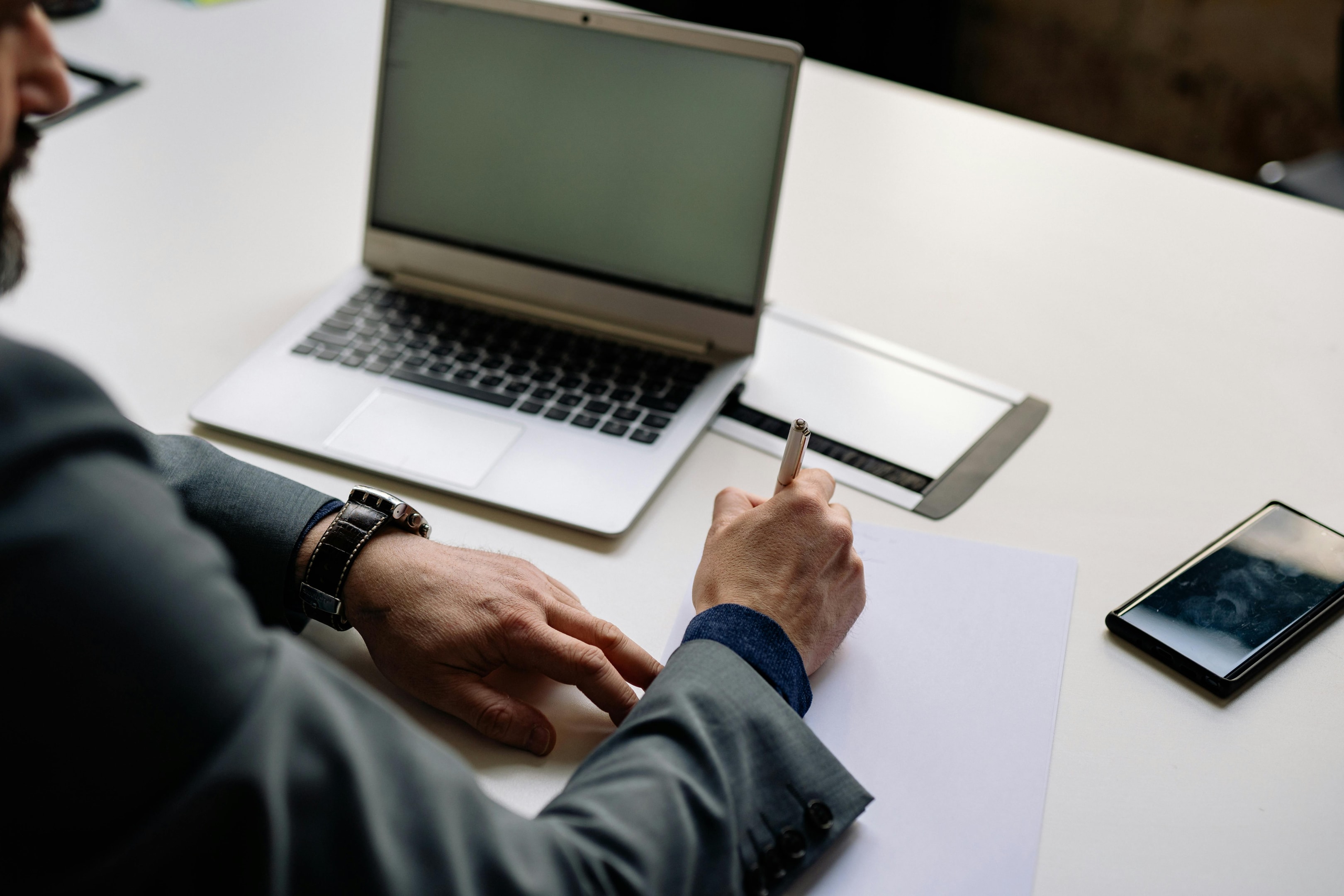 man writing down on paper by laptop