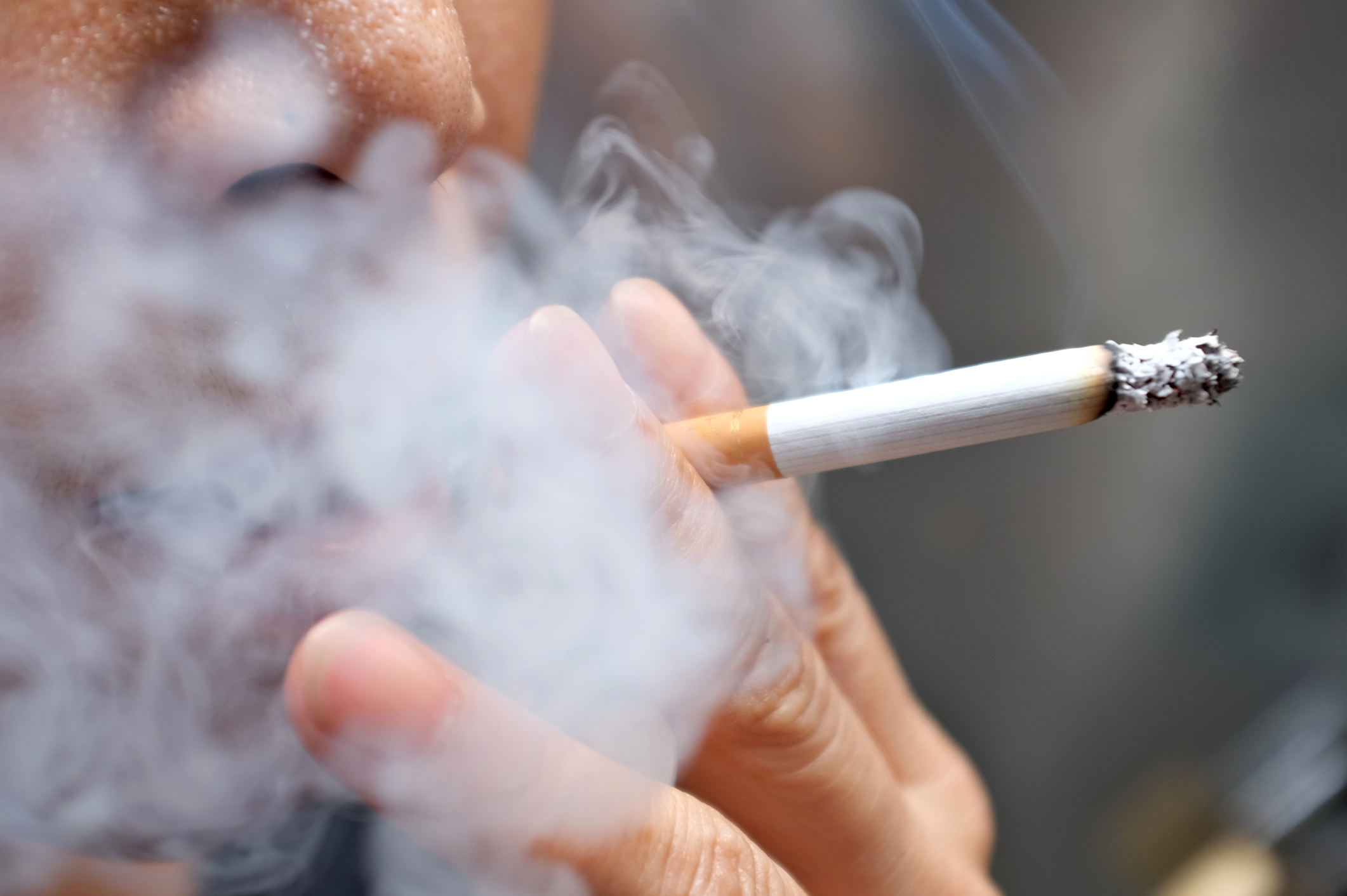 An image of a person smoking a cigarette, smoke swirling around their face. 