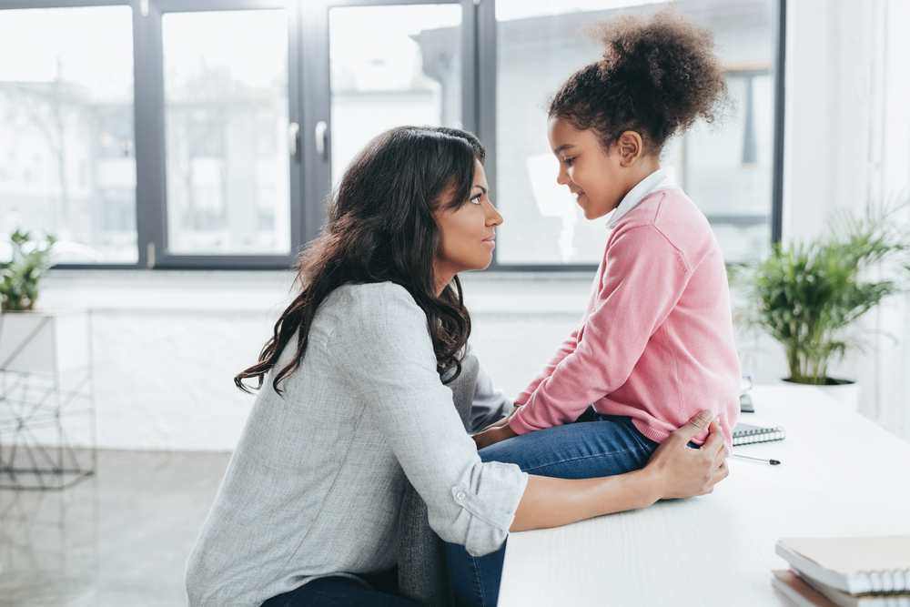 A mother kneeling down to talk face-to-face with a young girl