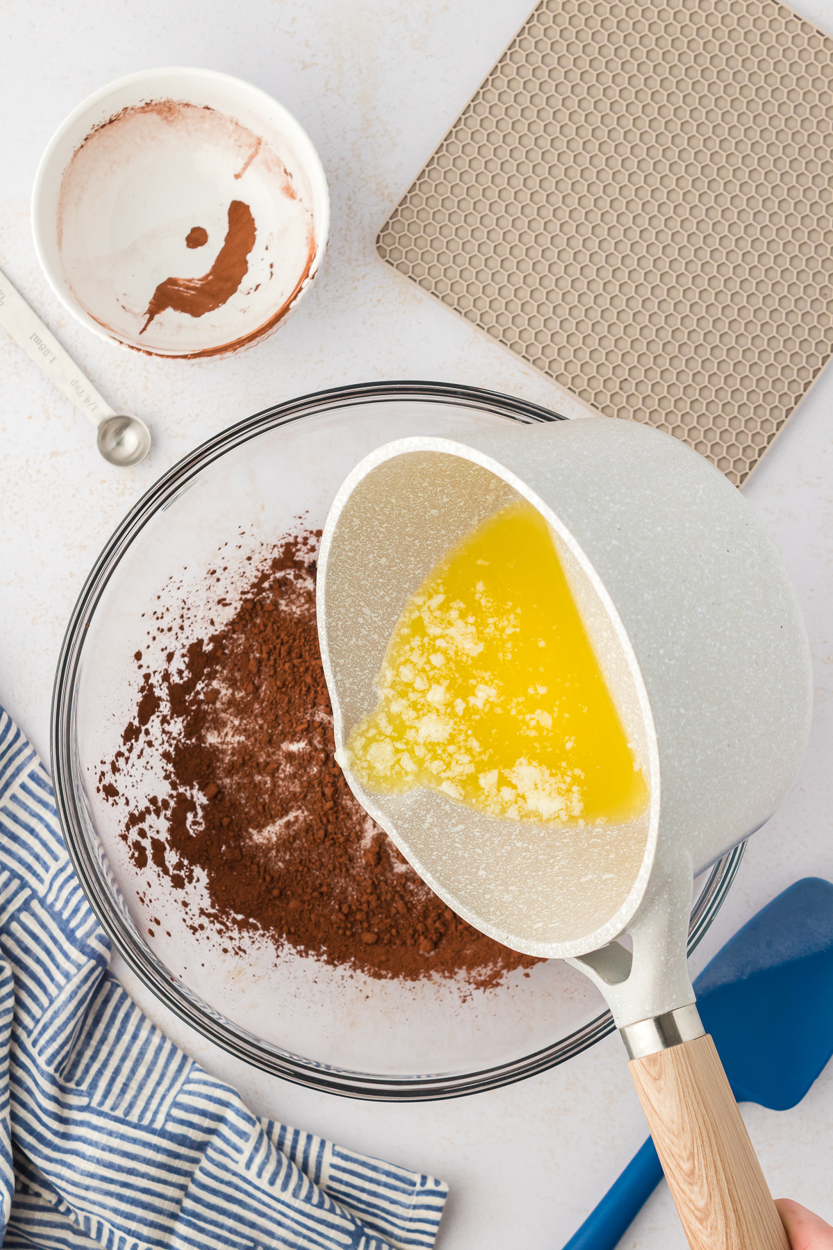 butter being poured into sugar, dark cocoa powder, and salt in large bowl