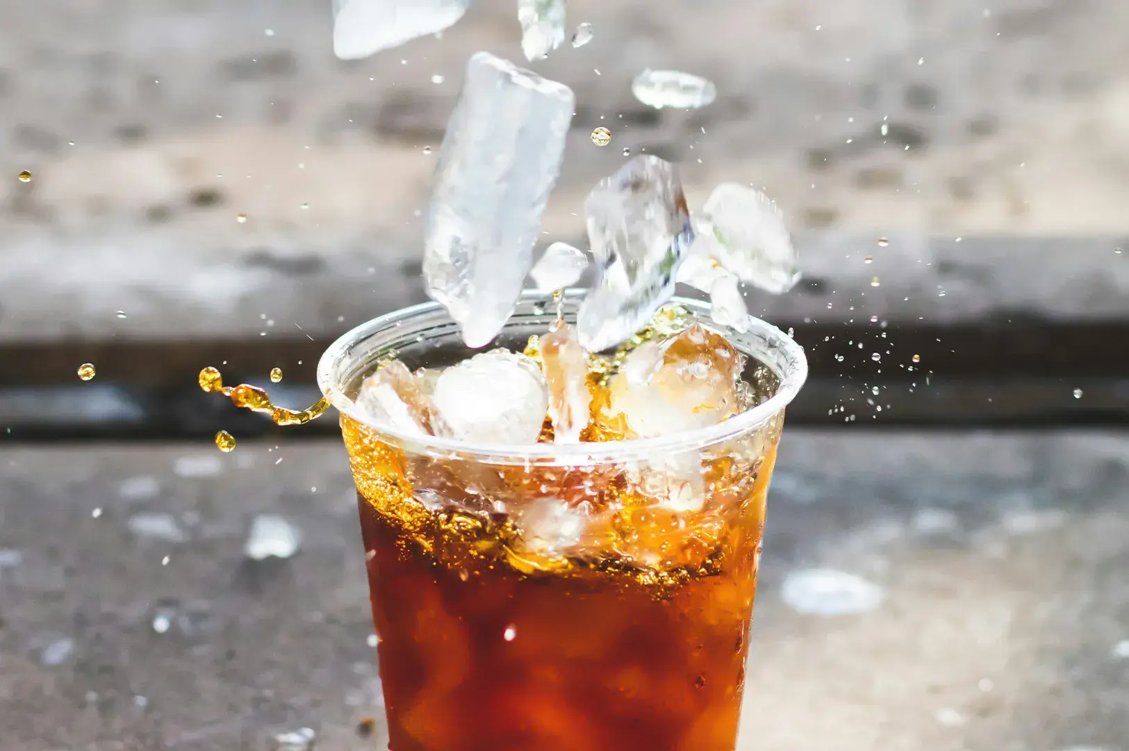Action photo of ice cubes splashing into iced tea in a plastic cup.