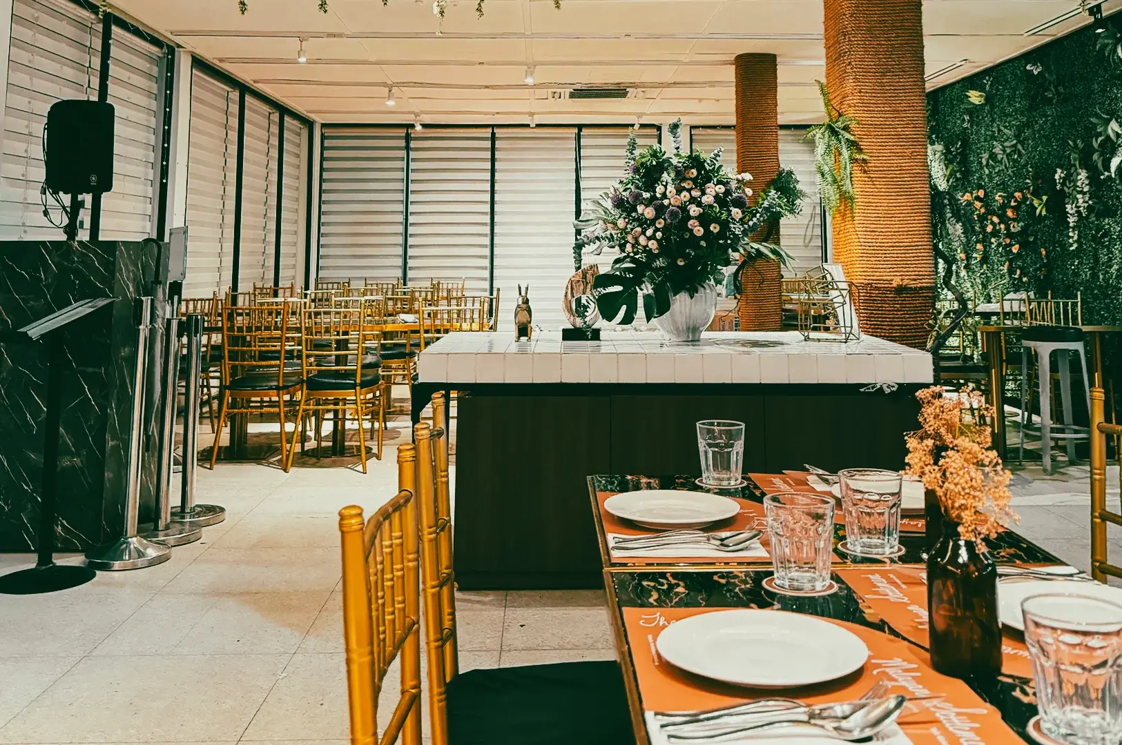 Wide-angle shot of a stylish halal restaurant dining space with neatly set tables, floral centerpiece, gold chairs, and modern interior design for group dining or events.