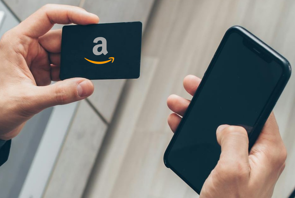 Person hand holding an Amazon gift card in left hand and smartphone in right hand