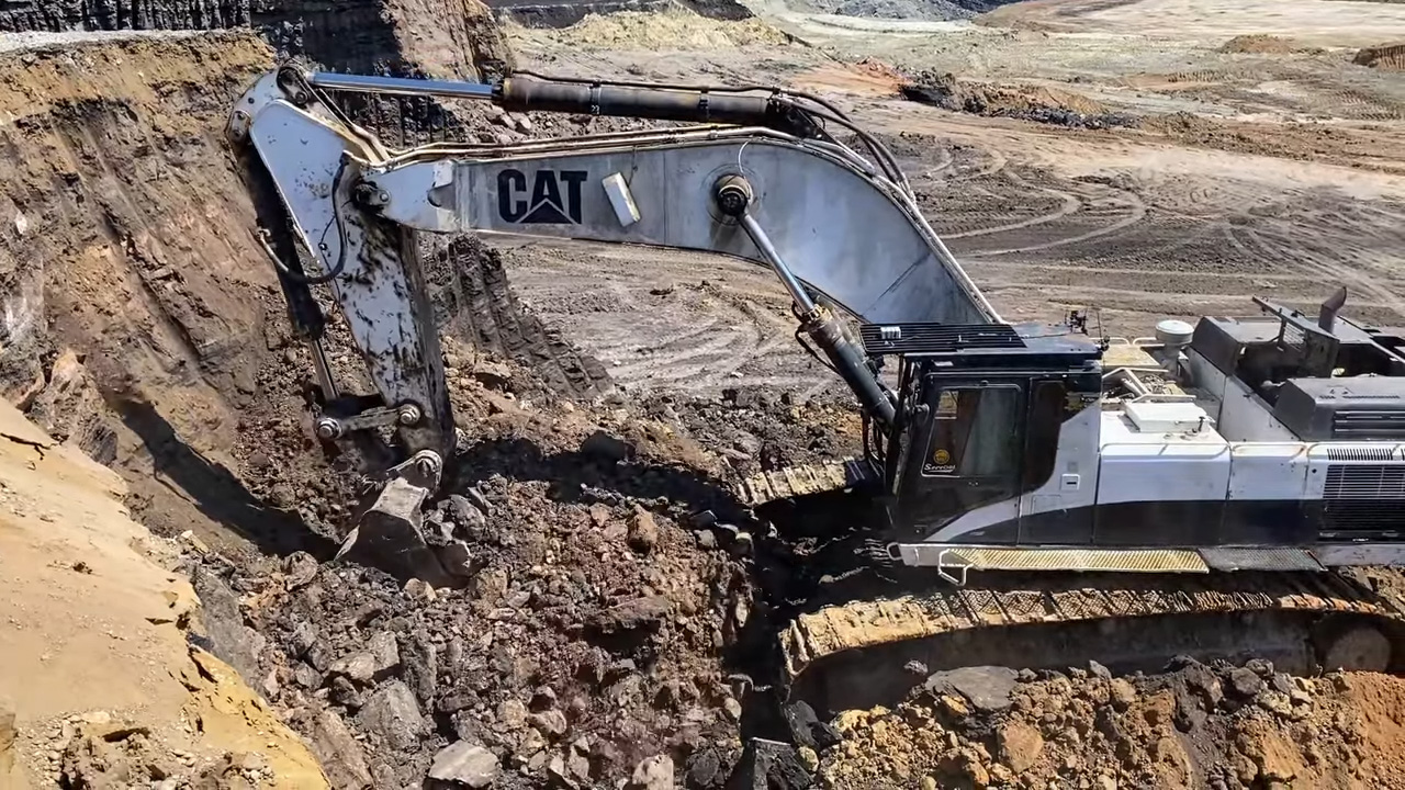 A Caterpillar excavator digging and moving dirt in a large outdoor mining site