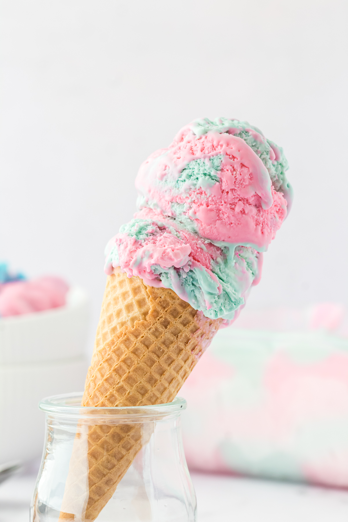 two scoops of cotton candy ice cream in waffle cone sitting in glass jar