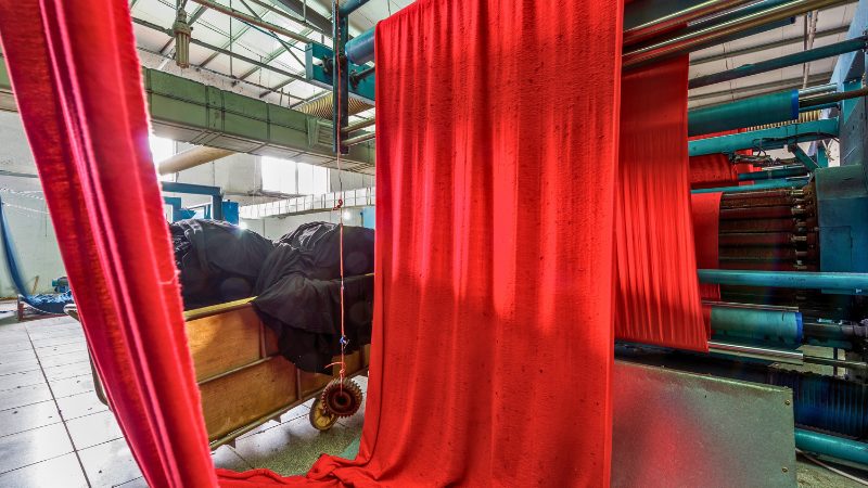 Large rolls of bright red fabric are being processed on machinery in a factory setting.