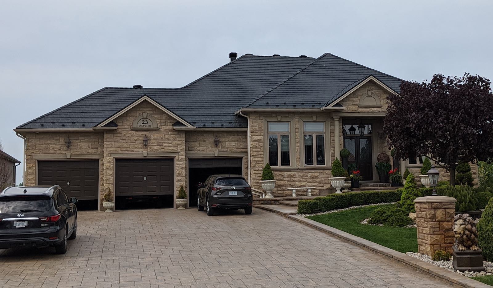 A picture of a home with a roof installed by Roof Pros Plus. The home is stone and the roof is a dark metal, highlighting the importance of choosing a roof colour that matches the aesthetic of the home.