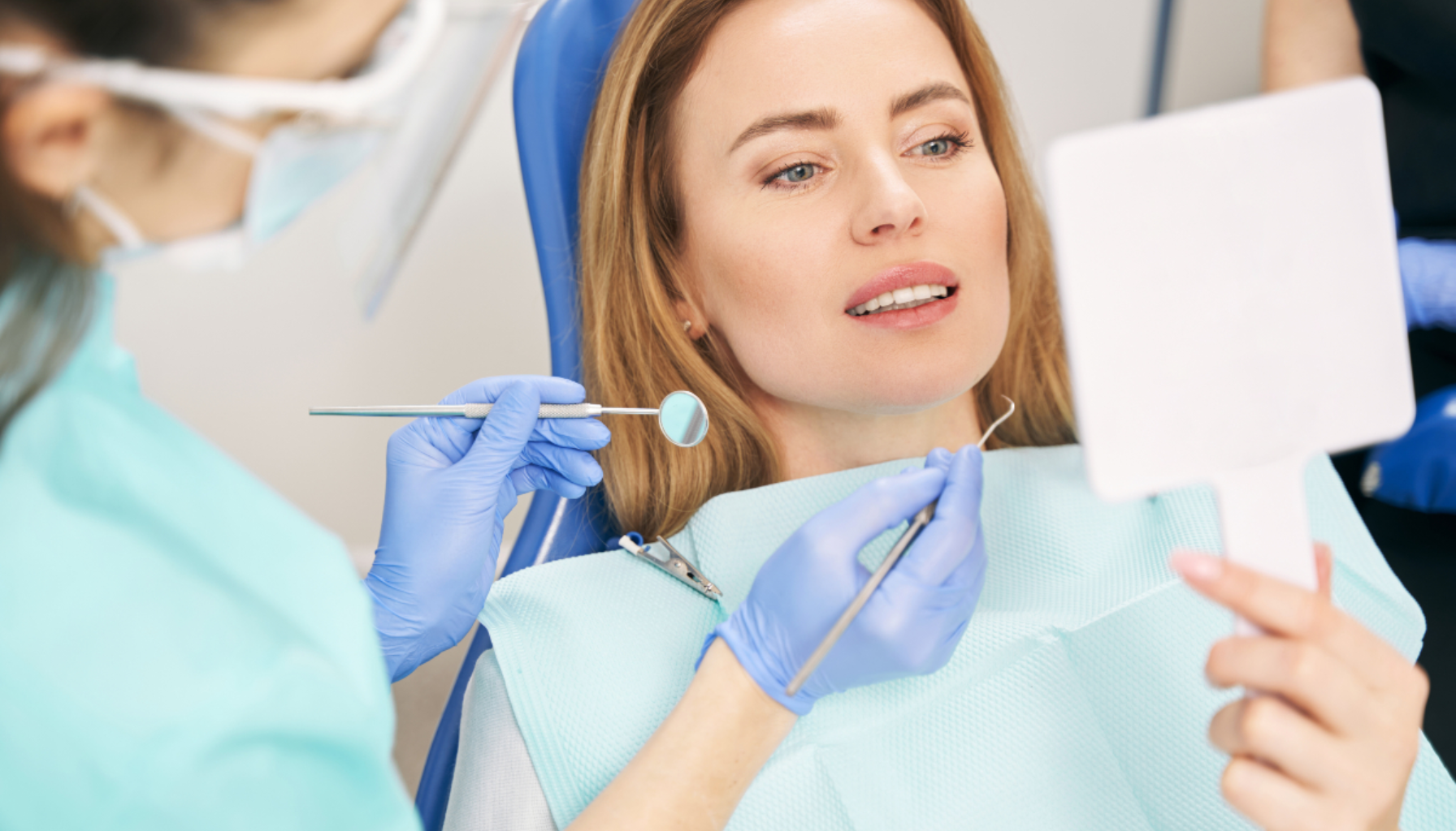 Kvinne i tannlegestol ser i speil mens tannlege med hansker og verktøy forklarer resultat etter tannbehandling i klinikk.