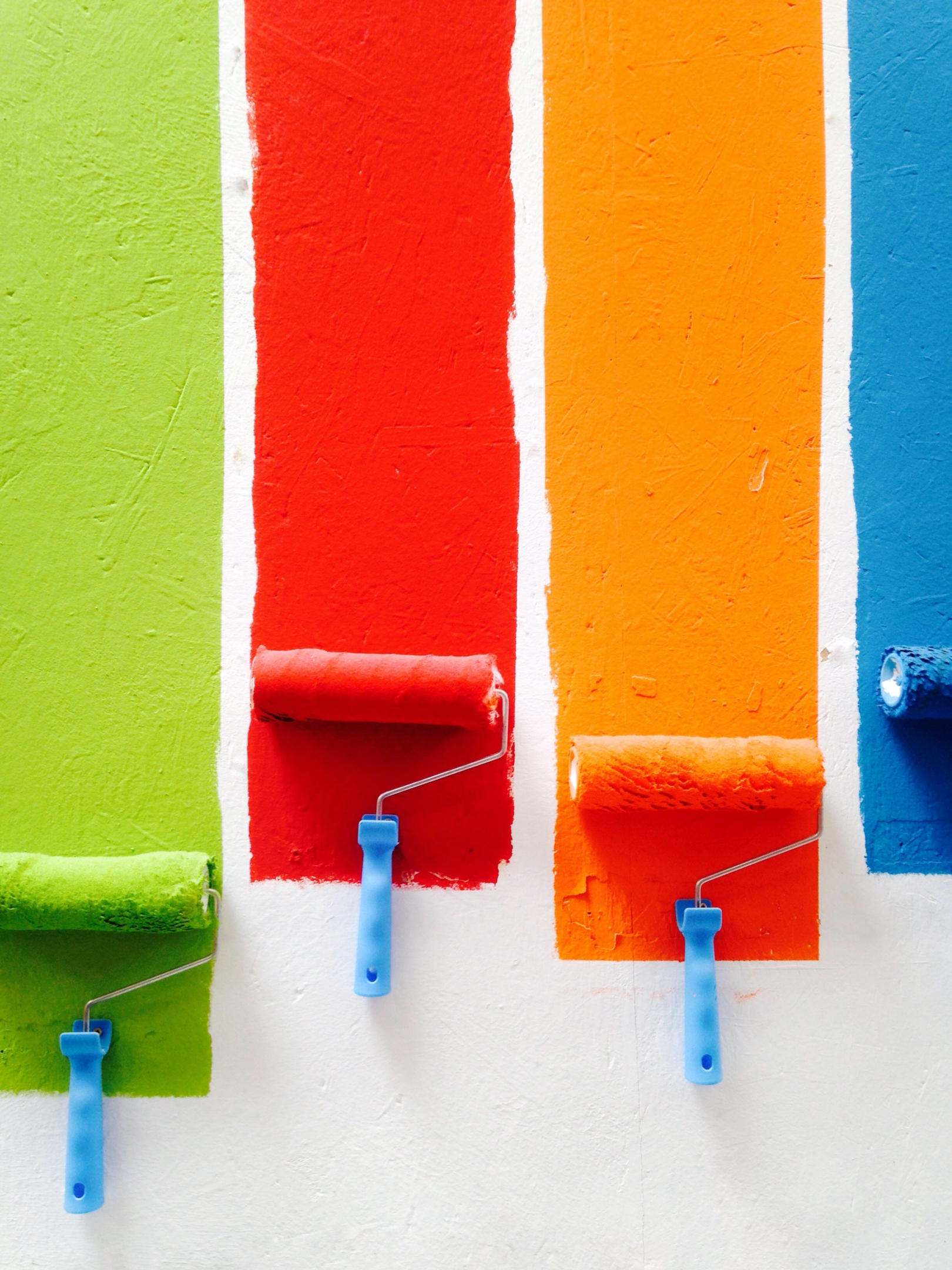 Paint rollers painting a white wall green, red, orange and red.