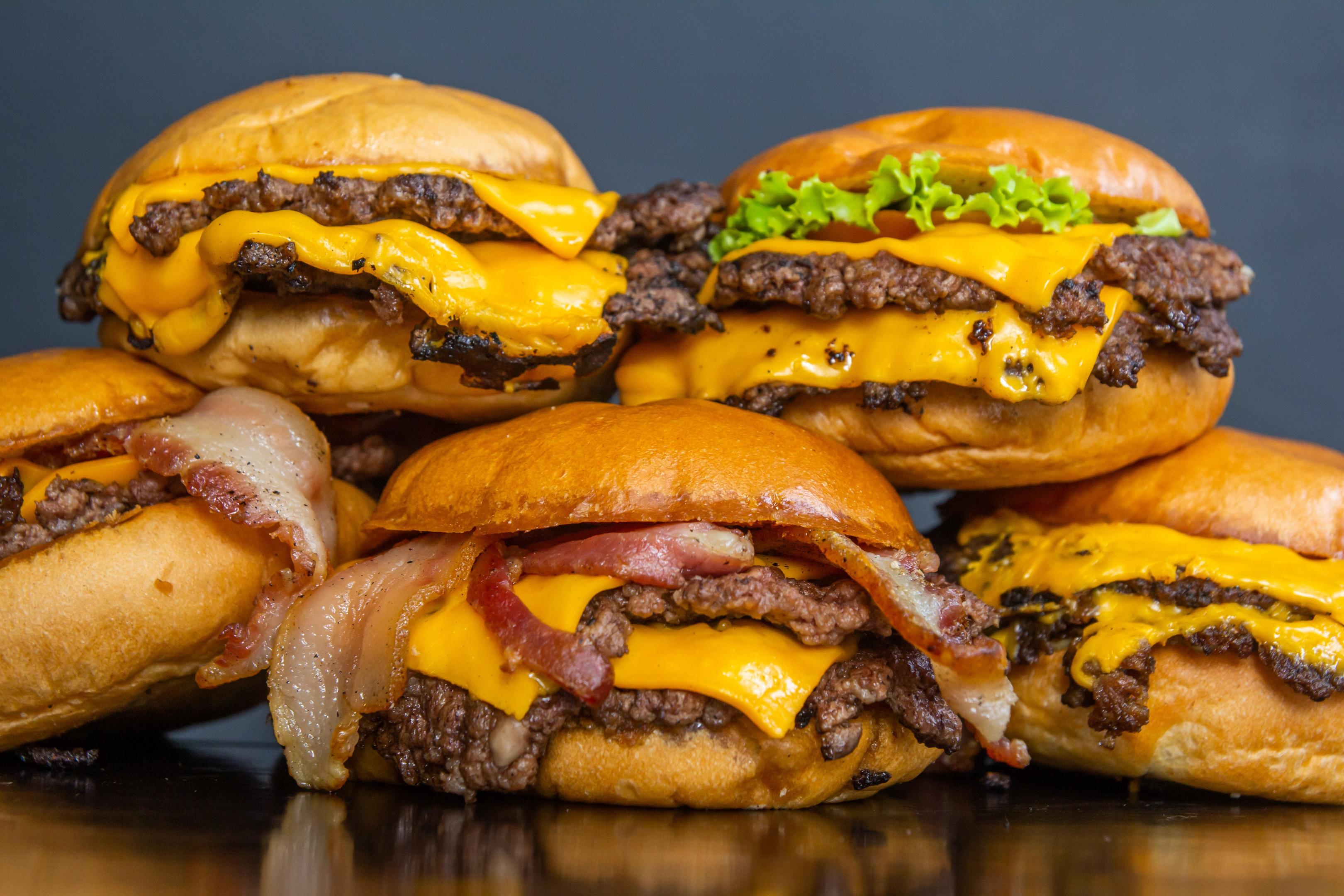 A close-up of loaded smashed burgers with melted cheese and vibrant toppings arranged on a rustic wooden board, highlighting current food trends in the restaurant industry.