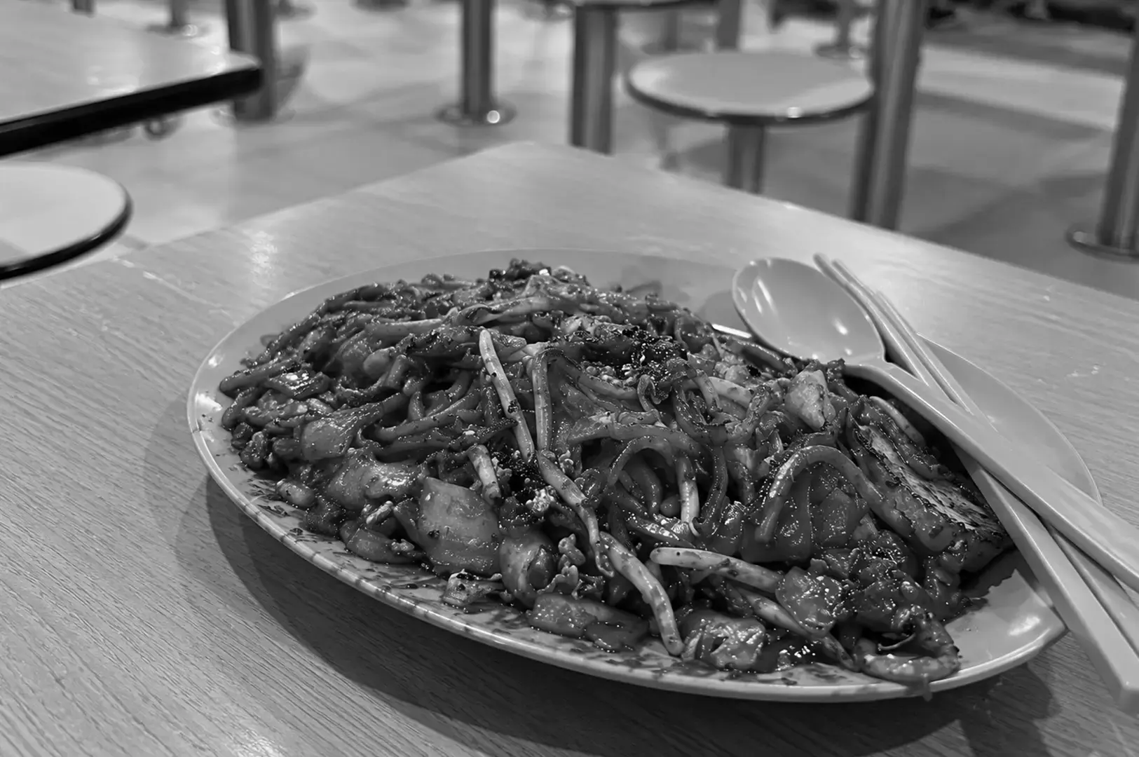 Char kway teow piled onto a plate, with flat rice noodles, bean sprouts, and chunks of ingredients coated in dark stir-fry sauce.