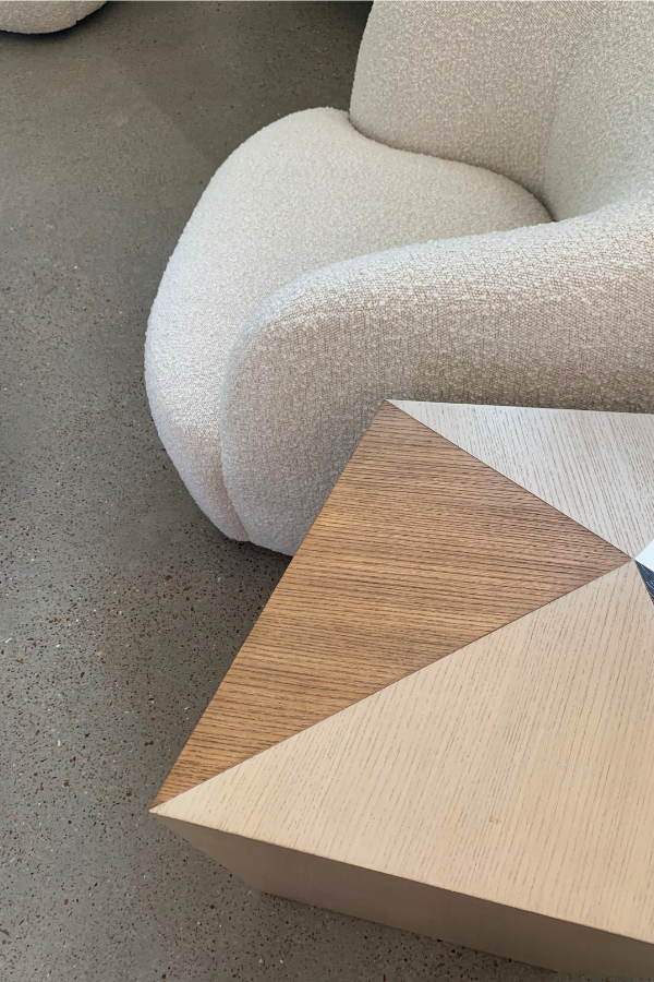 Close view of a cream boucle chair next to a geometric wood coffee table with mixed wood tones.