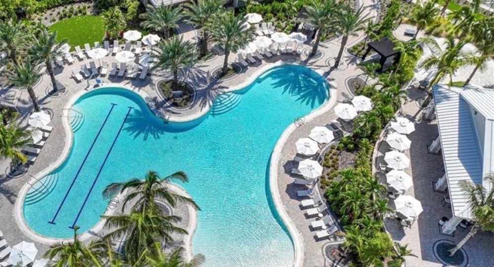 The image depicts a serene marina at the Esplanade Lake Club in Fort Myers, featuring private boat docks and picturesque waterfront walking paths surrounded by lush landscaping. This inviting space offers residents and visitors a perfect setting to enjoy an active lifestyle amidst the natural beauty of Southwest Florida.