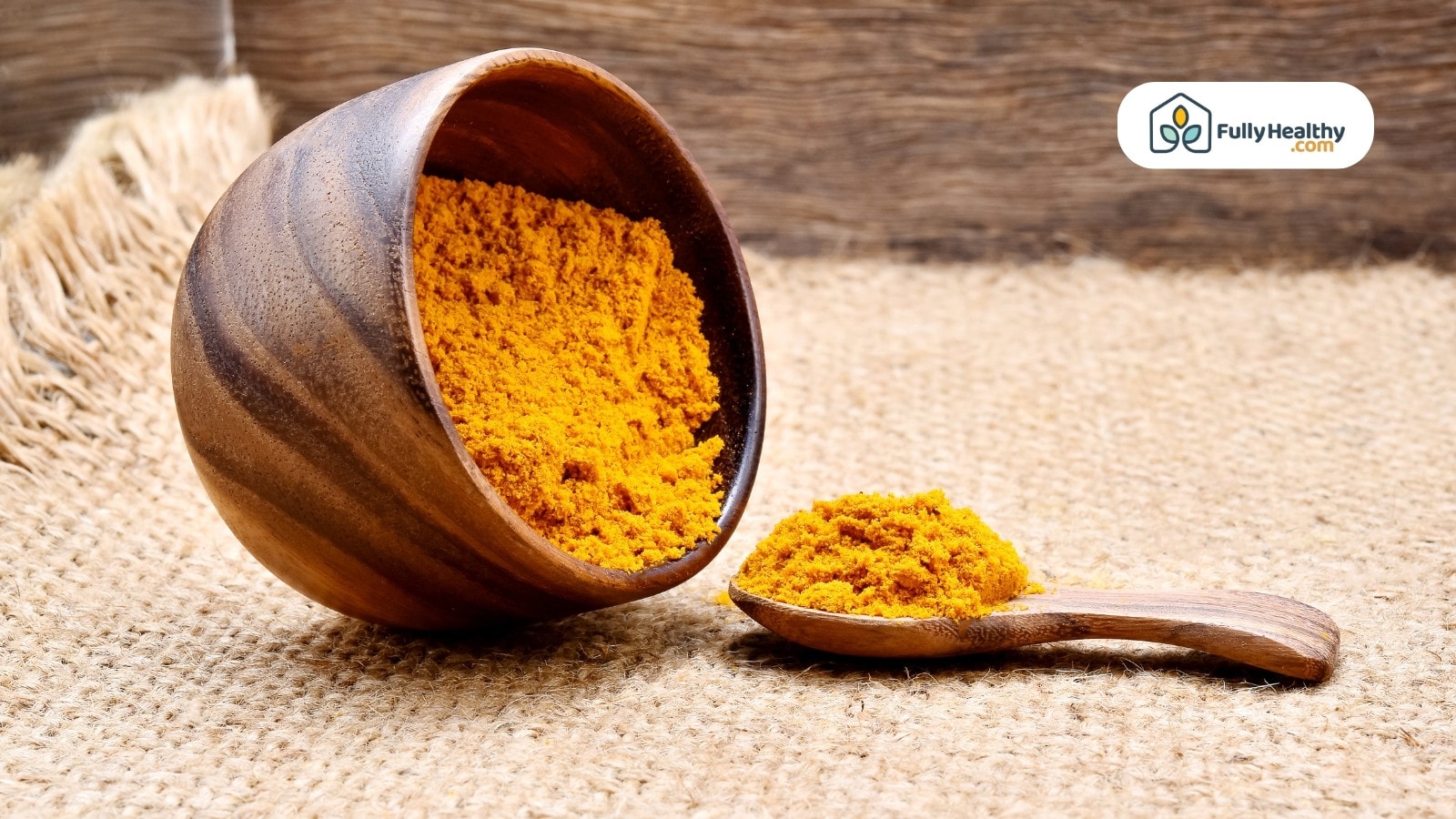 Wooden bowl and spoon filled with turmeric powder on jute surface