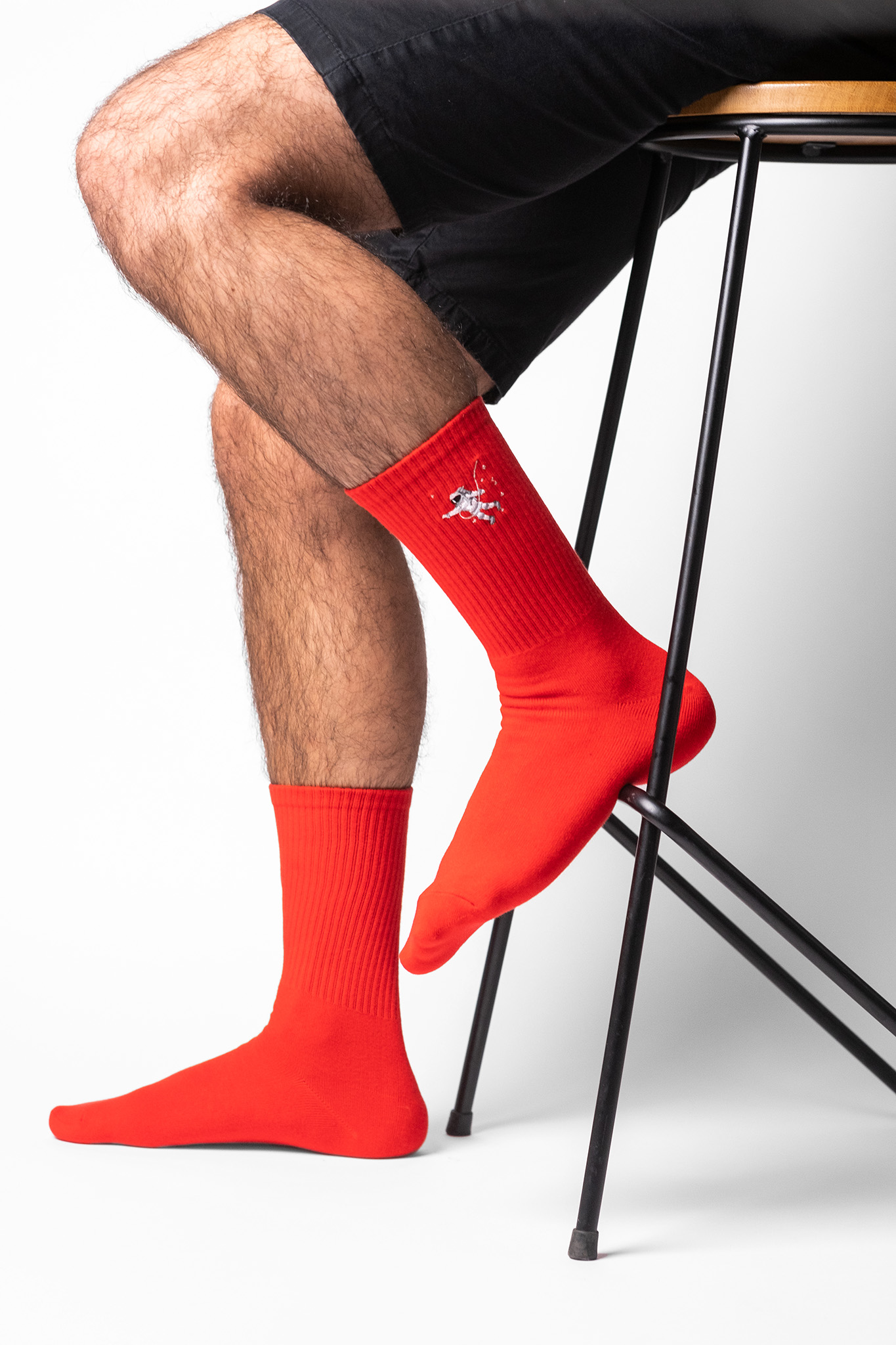 A male model wearing a pair of personalised red crew socks with the an astronaut embroidered onto each sock.