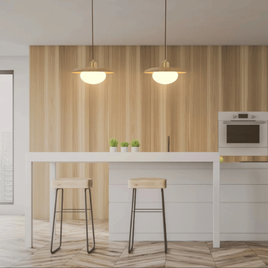 Two Japandi-style pendant light fixtures with brass accents and round glass shades, hanging above a minimalist kitchen island, creating a serene and modern atmosphere with warm, ambient light.