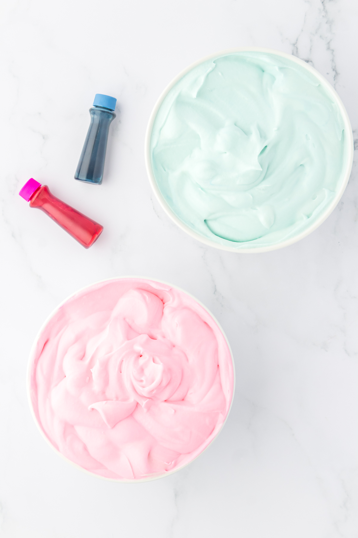 two bowls of cotton candy ice cream, one bowl is pink and one is blue, and two bottles of food coloring