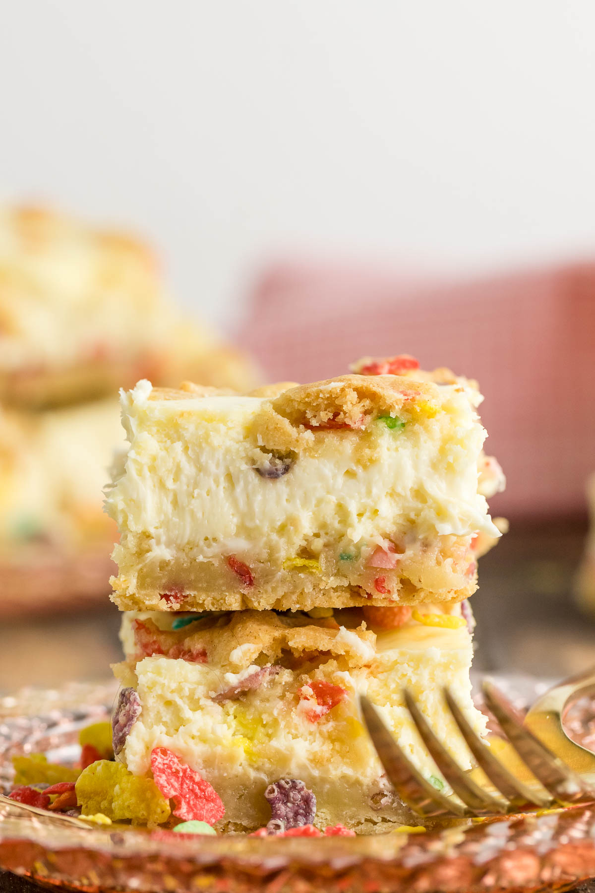 two fruity pebble cheesecake bars stacked on a plate with a fork