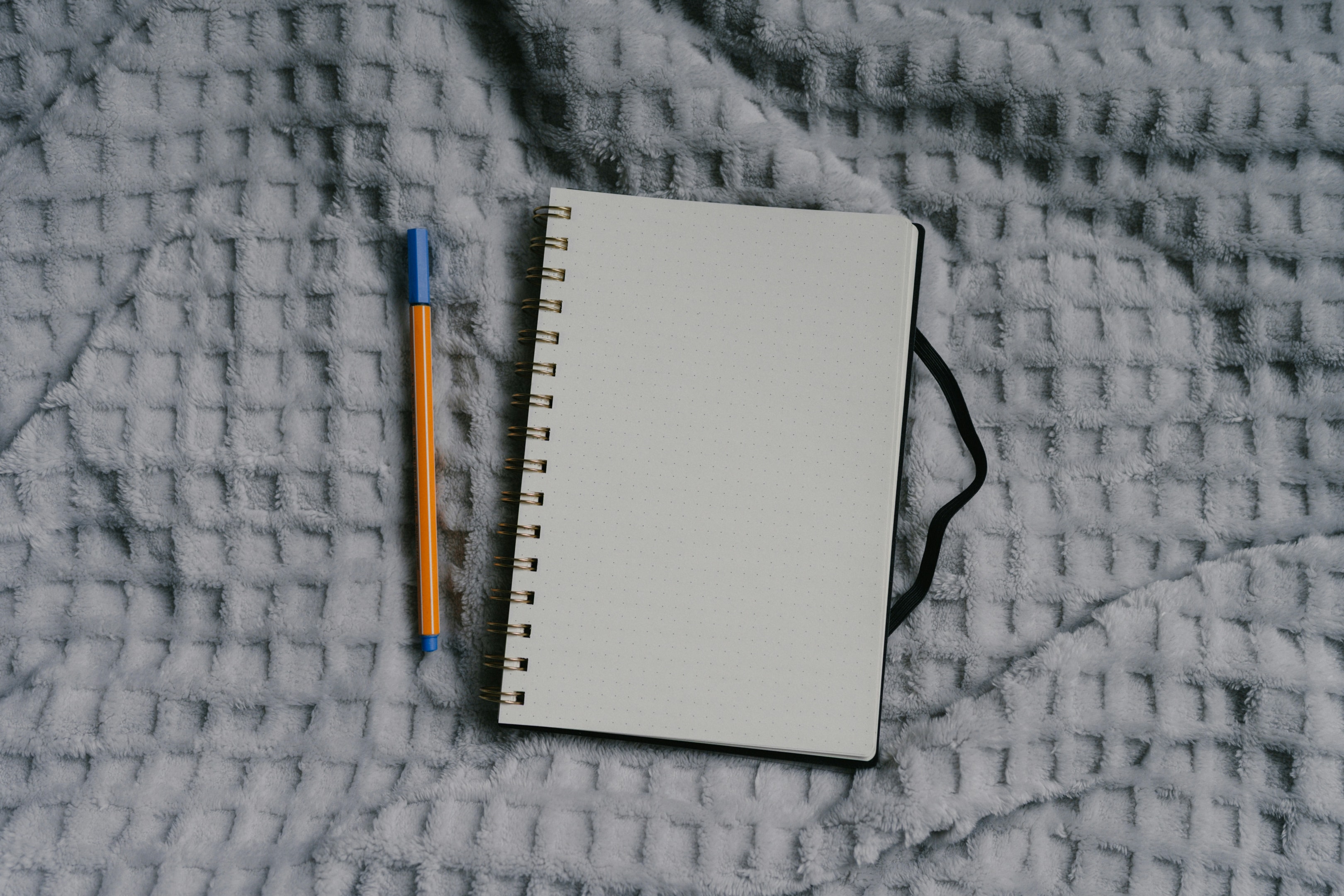 A blank notebook and pen on a bed.