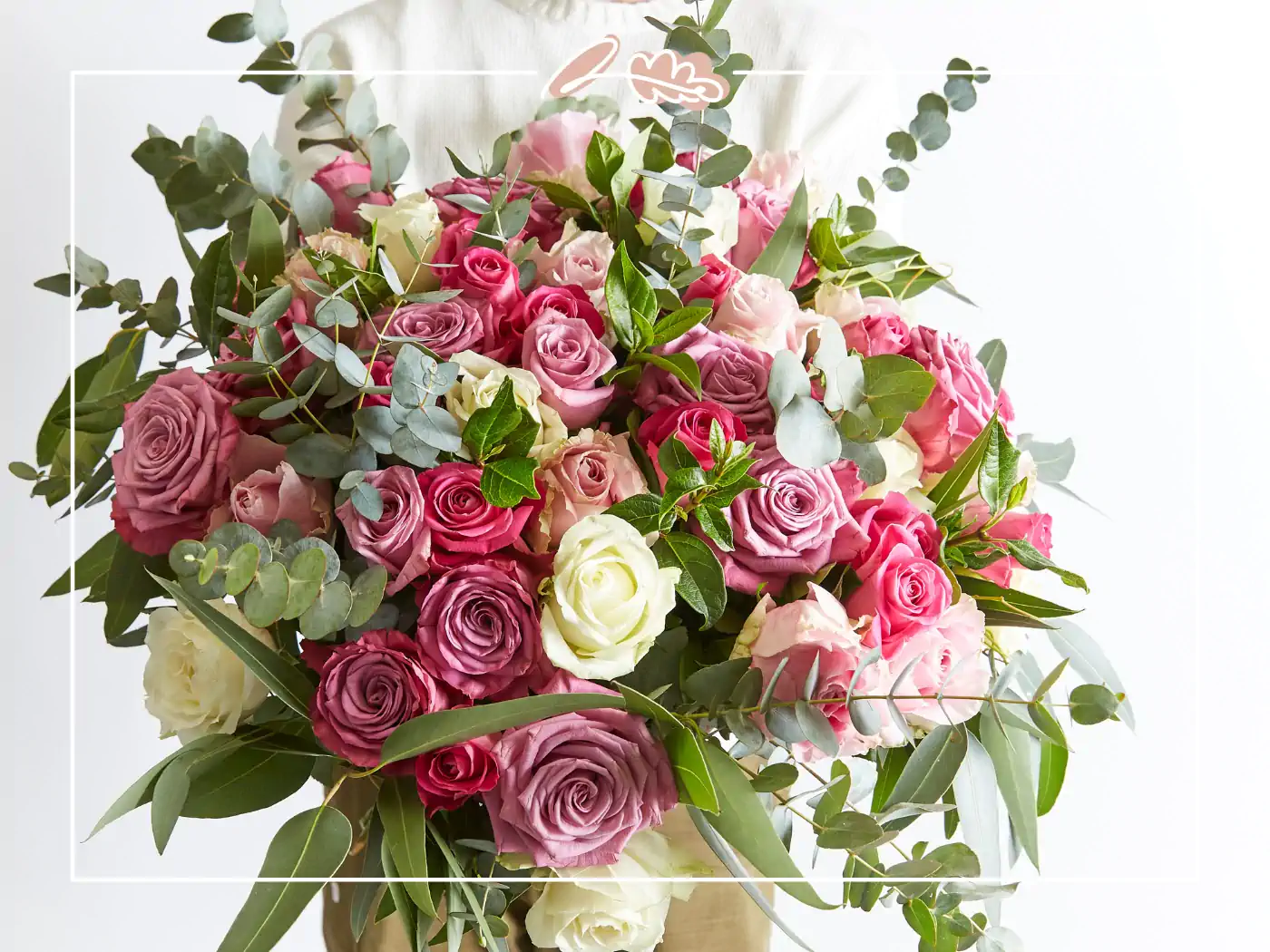 A stunning bouquet of pink and white roses with lush green foliage, expertly arranged and held by a person wearing a white shirt. Fabulous Flowers and Gifts.