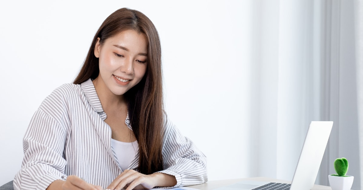 Woman smiling while conducting a risk audit on her laptop in a bright, white office space.