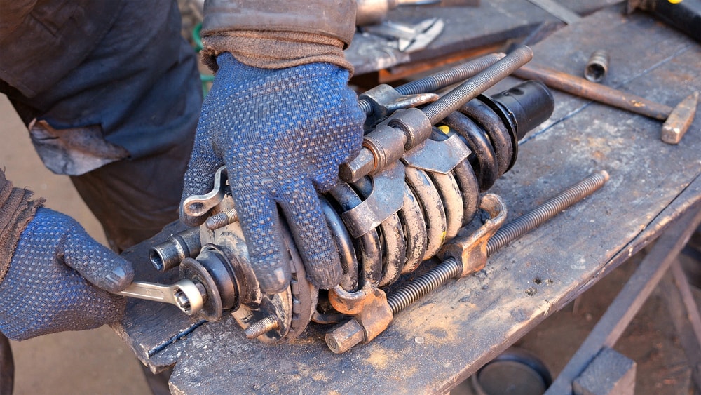 Работник в автосервиз със сини работни ръкавици работи по поправката на амортисьор