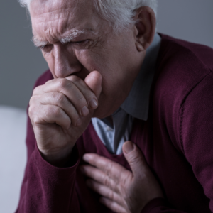 An image of a senior man with his fist over his mouth choking on food.