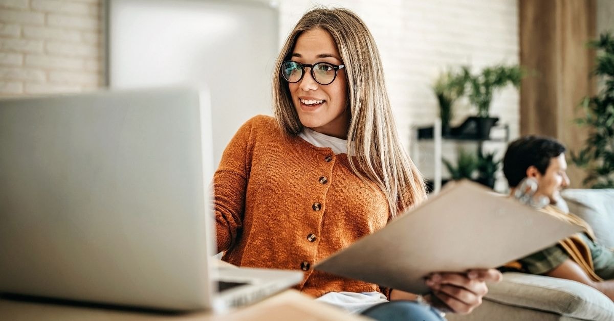 A smiling woman using her laptop to prepare for tax time, holding financial documents.