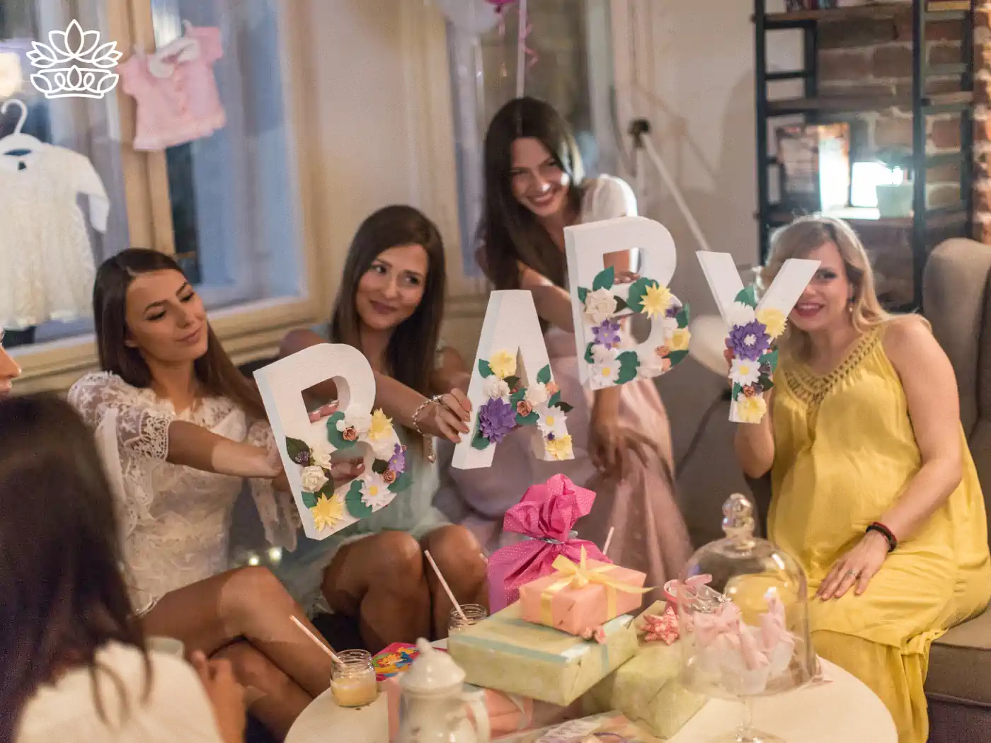 Group of women holding large letters spelling "BABY" decorated with colourful flowers, enjoying a baby shower celebration. Fabulous Flowers and Gifts: Baby Shower Flowers Collection