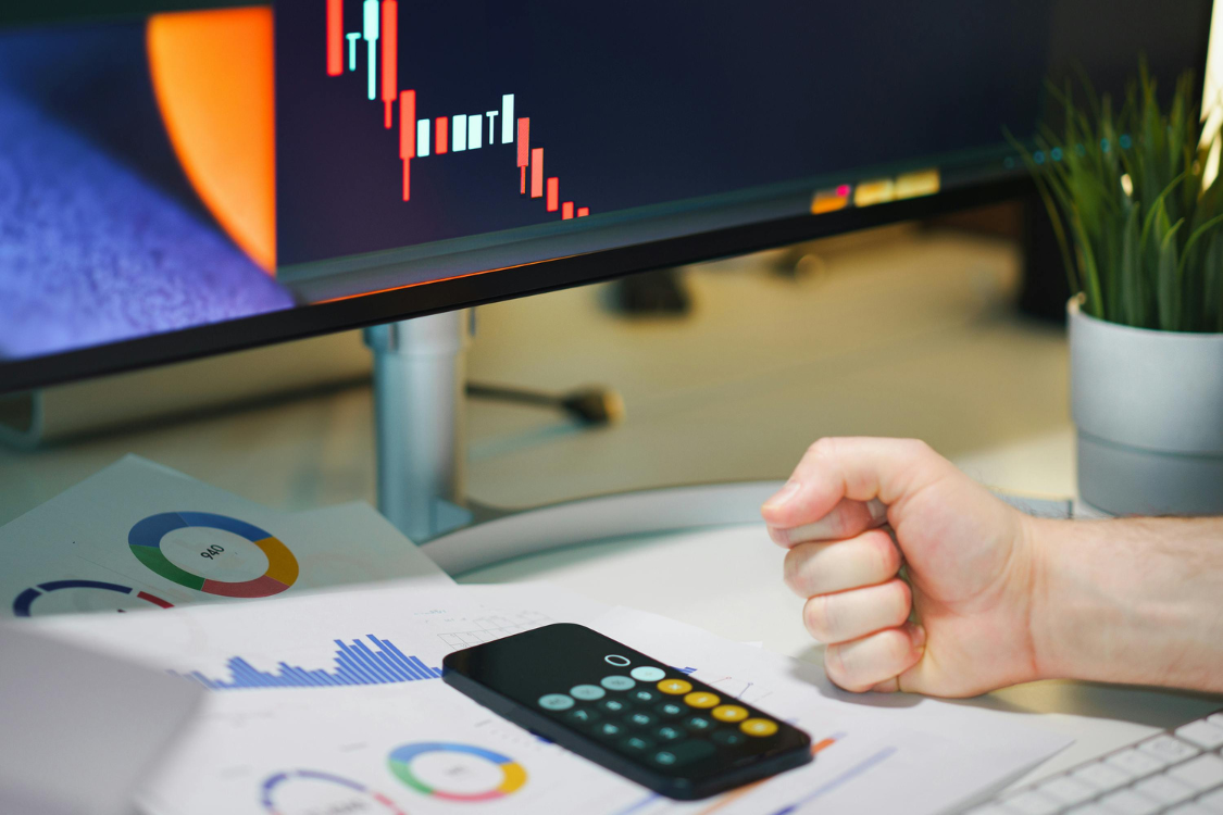Hand clenched in frustration in front of a screen showing financial losses and a declining stock chart