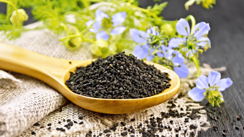 Schwarzkümmelsamen auf einem Löffel mit Blüten im Hintergrund